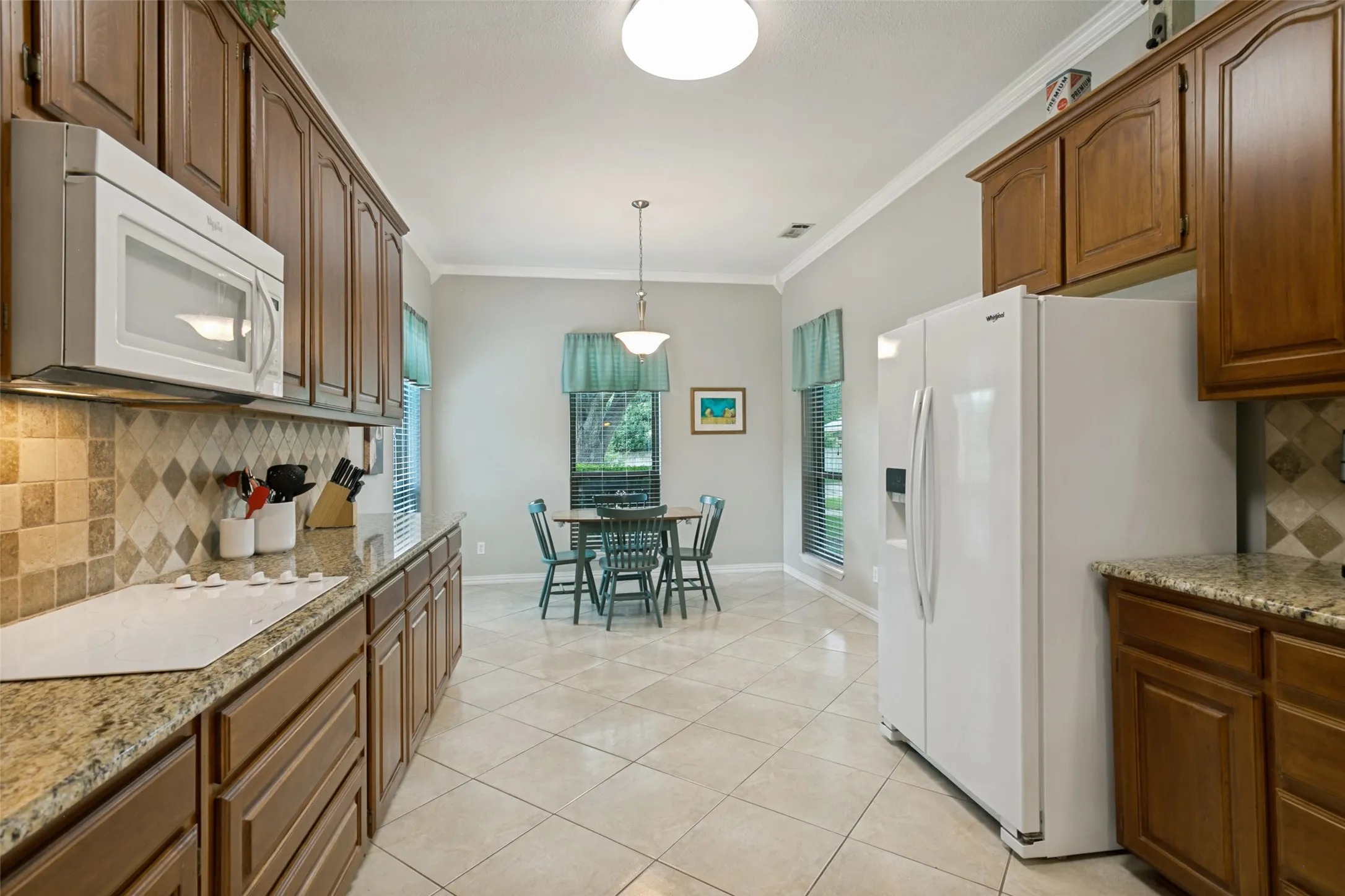 Rich oak cabinetry, granite countertops, patterned tile backsplash, recessed lighting, and tile flooring