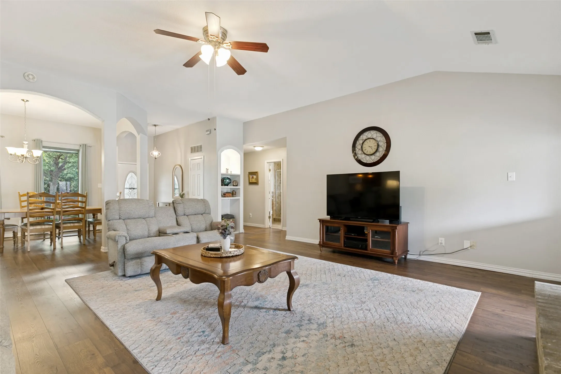 Vaulted ceiling with a ceiling fan, wood-finish flooring, recessed built-in shelving, and arched doorways
