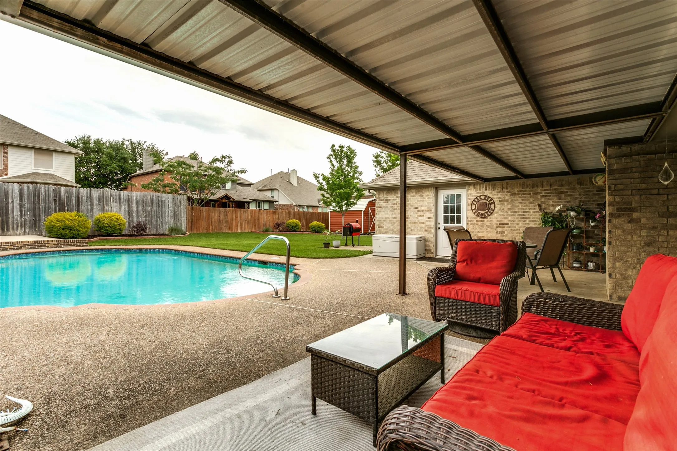 Covered patio with a corrugated metal roof, brick exterior wall, and concrete flooring