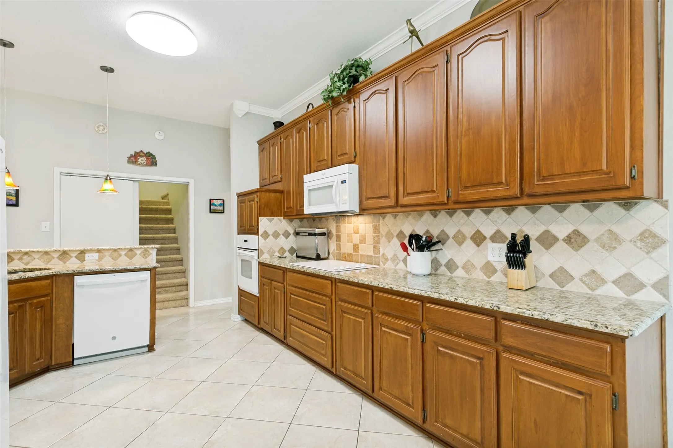 Oak cabinetry with crown molding, light-toned granite countertops, and a tiled backsplash with diamond accents