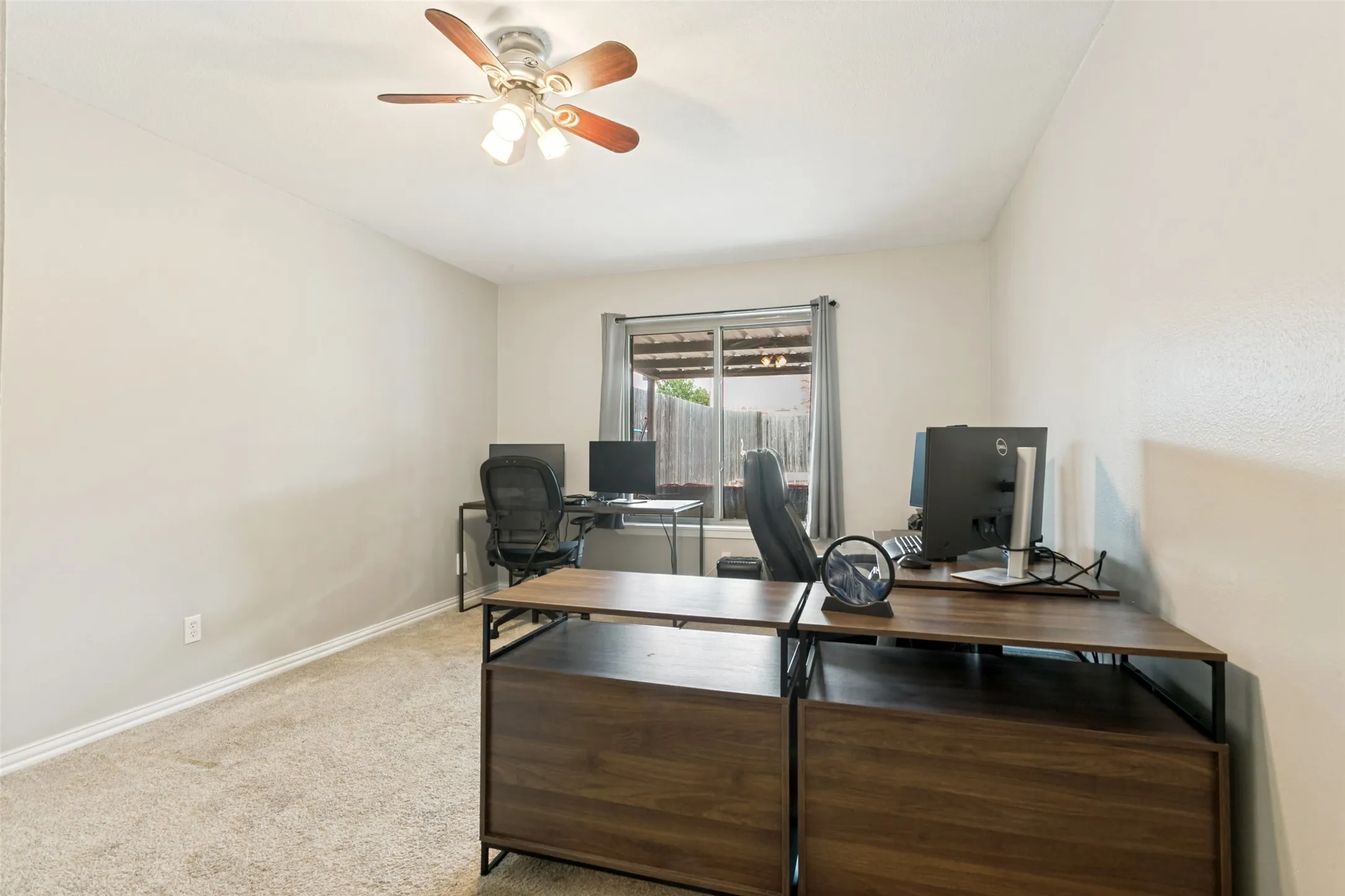 Neutral-toned walls, carpet flooring, a window with curtains, and a ceiling fan with integrated lighting
