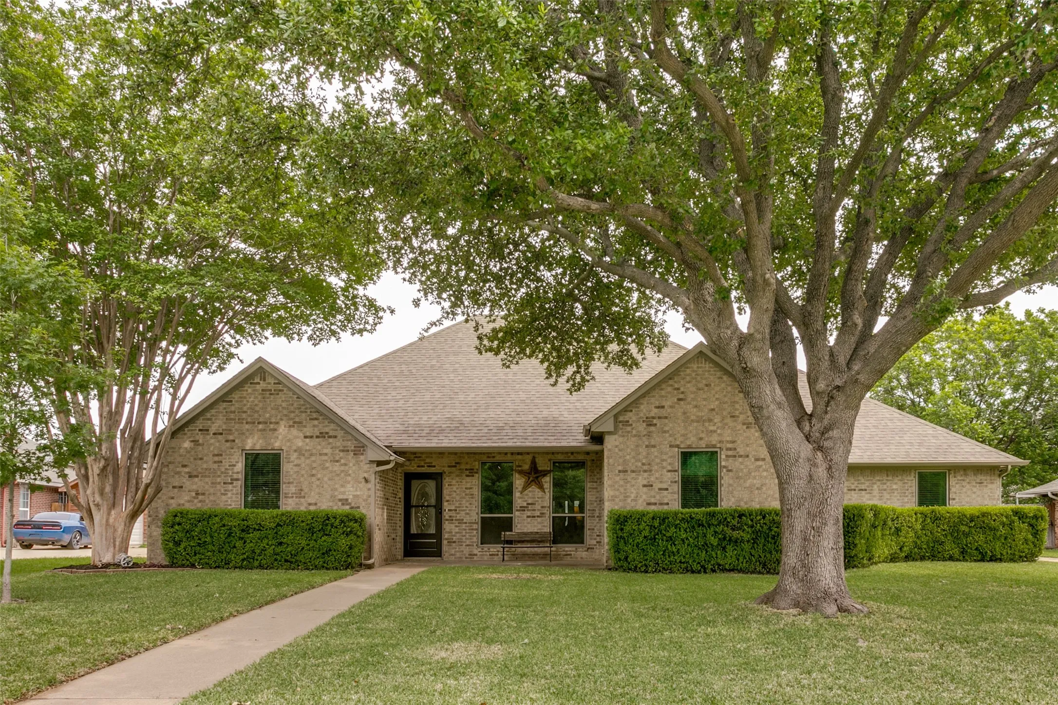 Brick exterior, mature trees, and a concrete pathway
