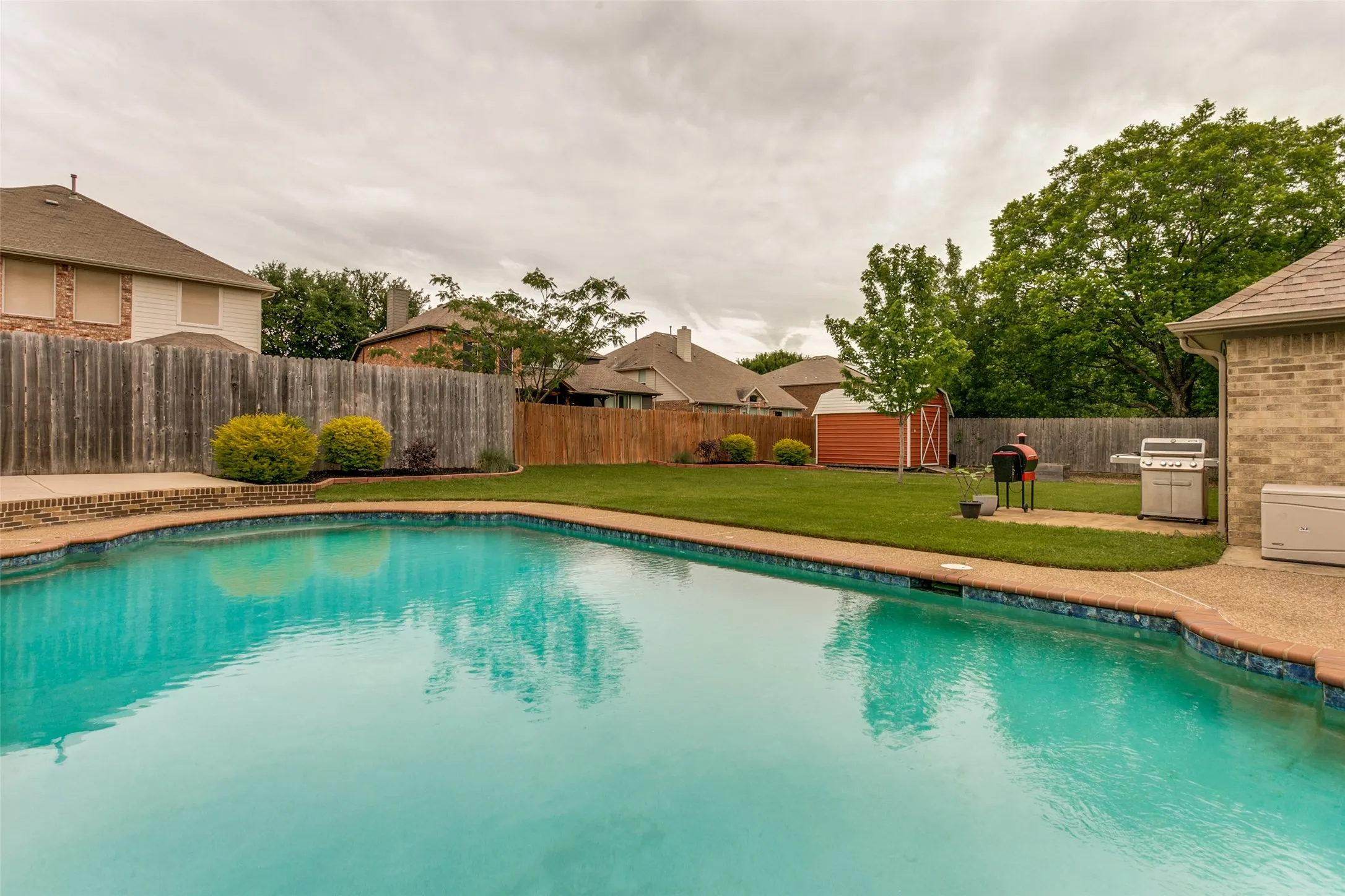 Expansive backyard featuring a swimming pool with a tiled coping, a manicured lawn, and a privacy fence