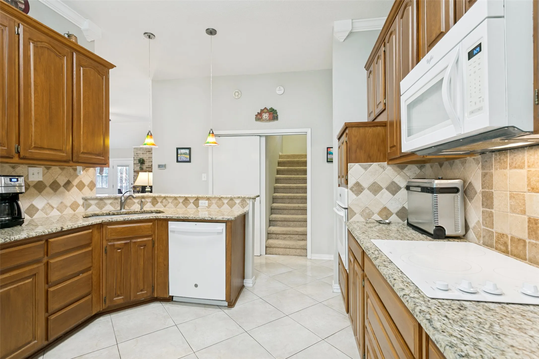 Kitchen featuring oak cabinetry, granite countertops, tile backsplash, built-in microwave, and pendant lighting