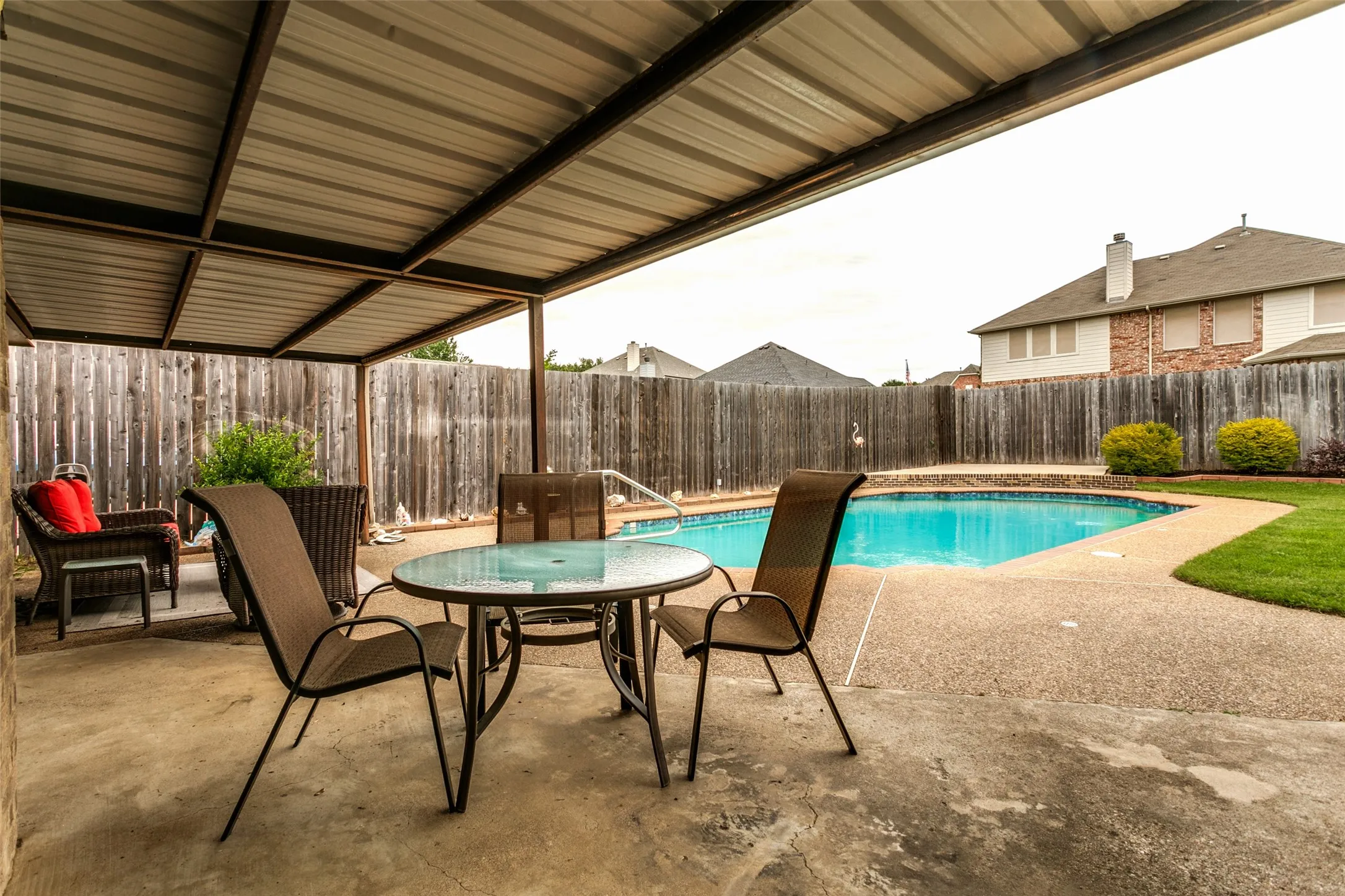 Covered patio with a corrugated metal roof, concrete patio, privacy fencing, and an in-ground swimming pool