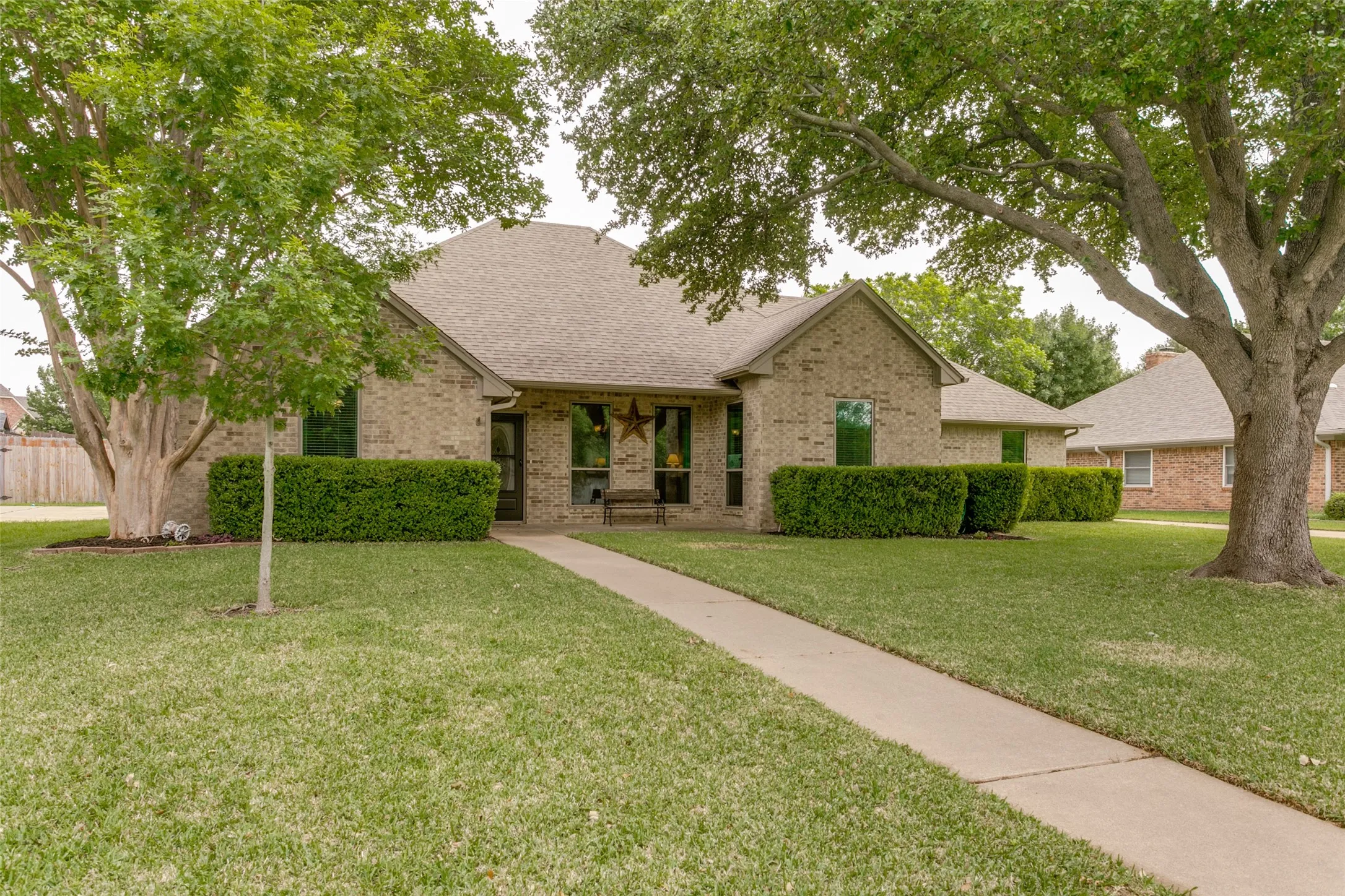 Brick exterior, mature trees, manicured shrubs, and a concrete walkway