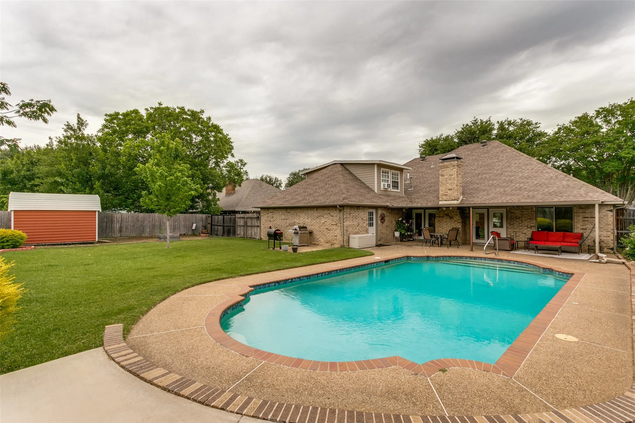 Curved swimming pool with a stone deck, expansive grassy lawn, and a detached storage shed