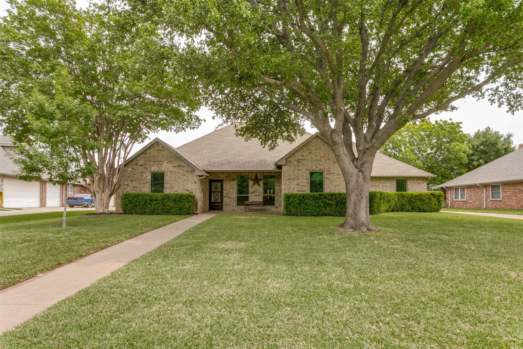 Brick exterior, mature trees, manicured lawn, and a concrete walkway