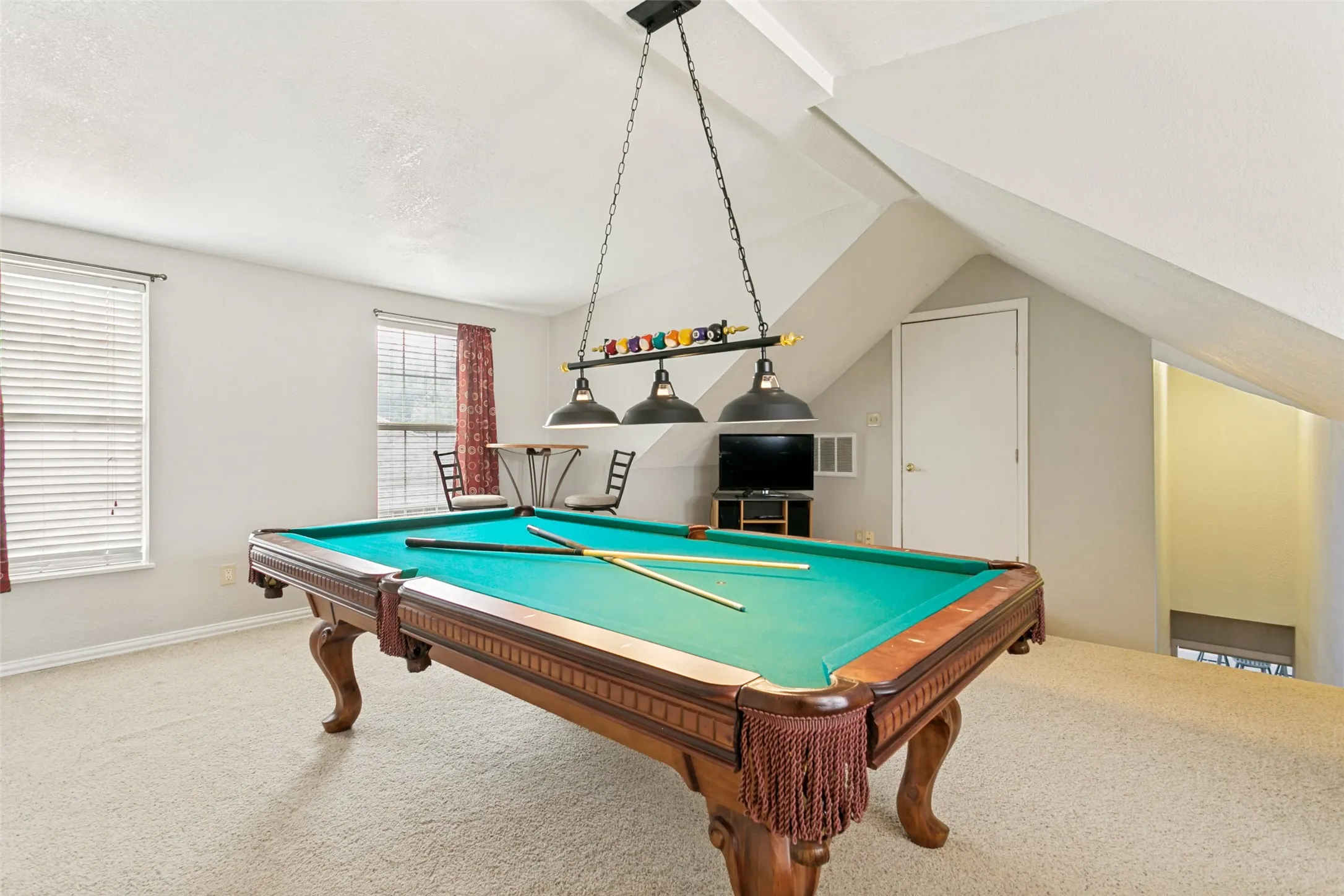 Carpeted room featuring a ceiling-mounted light fixture, two windows with blinds, an angled ceiling, and a built-in door