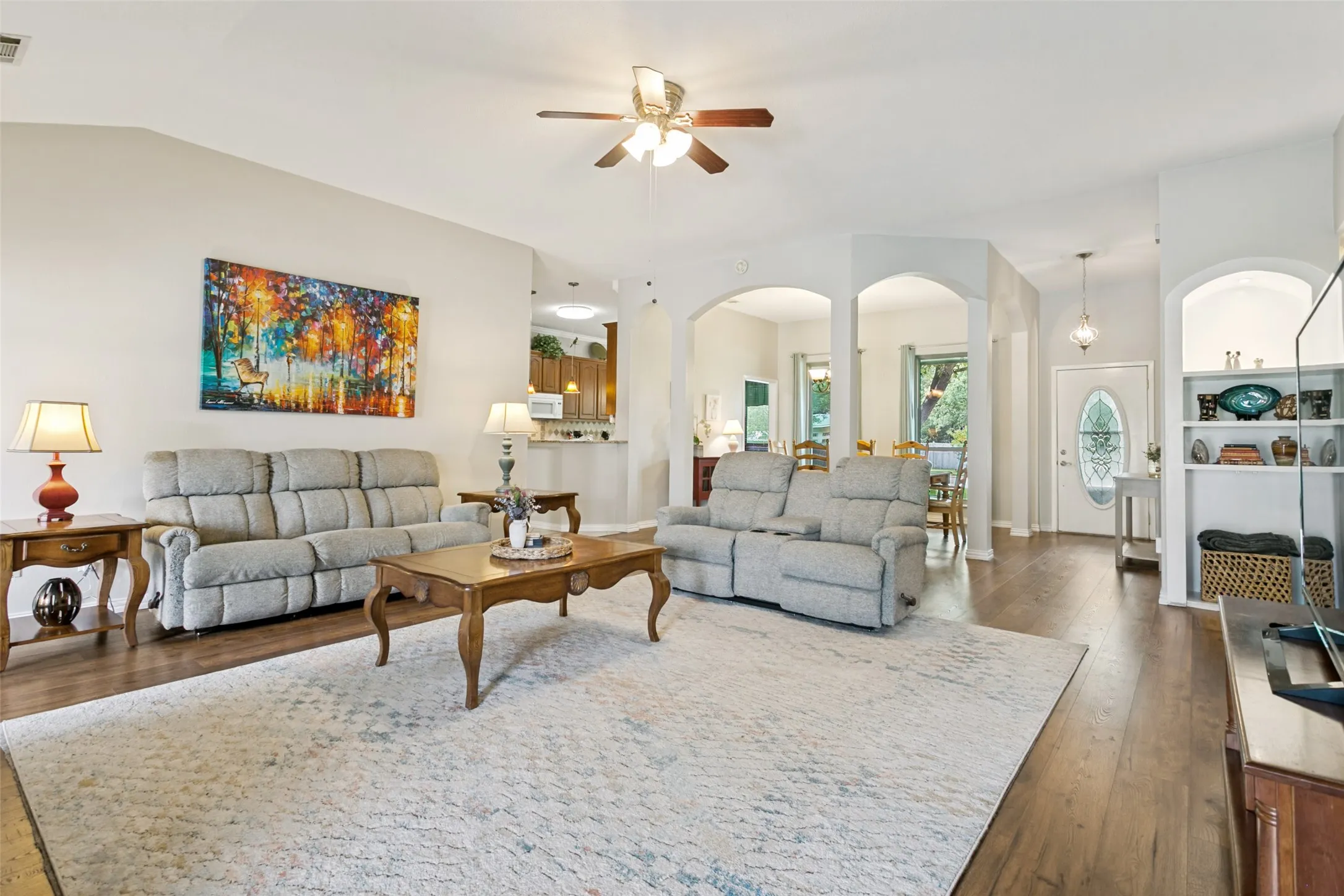 Vaulted ceiling with a ceiling fan, wood-finish flooring, arched doorways, built-in shelving, and a decorative front door with an oval glass insert
