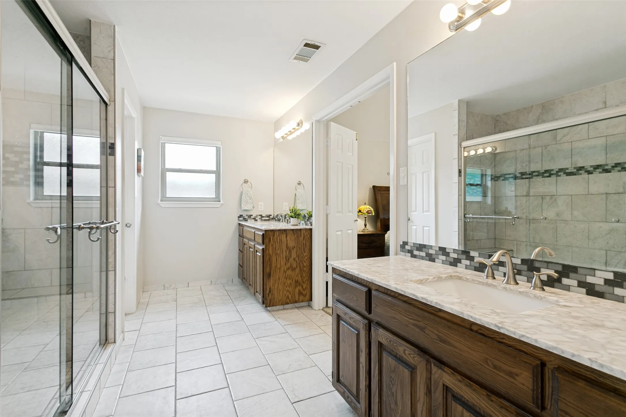Spacious bathroom featuring a glass-enclosed shower, dual oak vanities with undermount sinks, and a large wall mirror