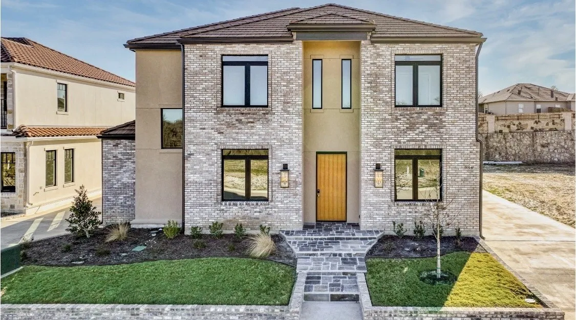 Stone facade with stucco accents, dark-framed windows, wood-finish entry door, and a stone walkway