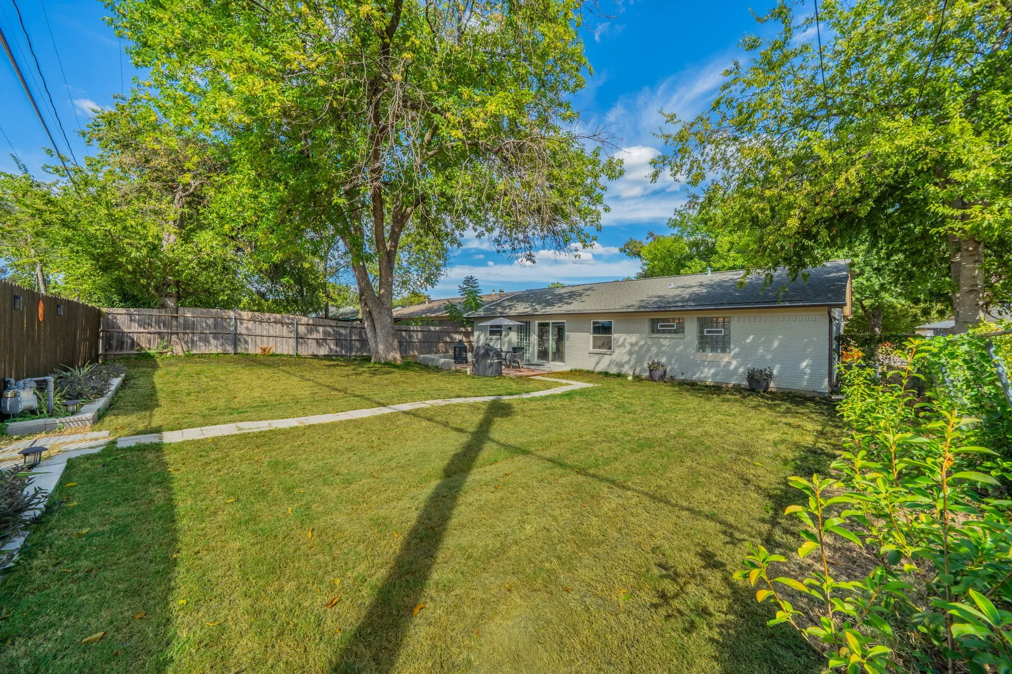 Expansive lawn area with a defined pathway, mature trees, and a wooden privacy fence