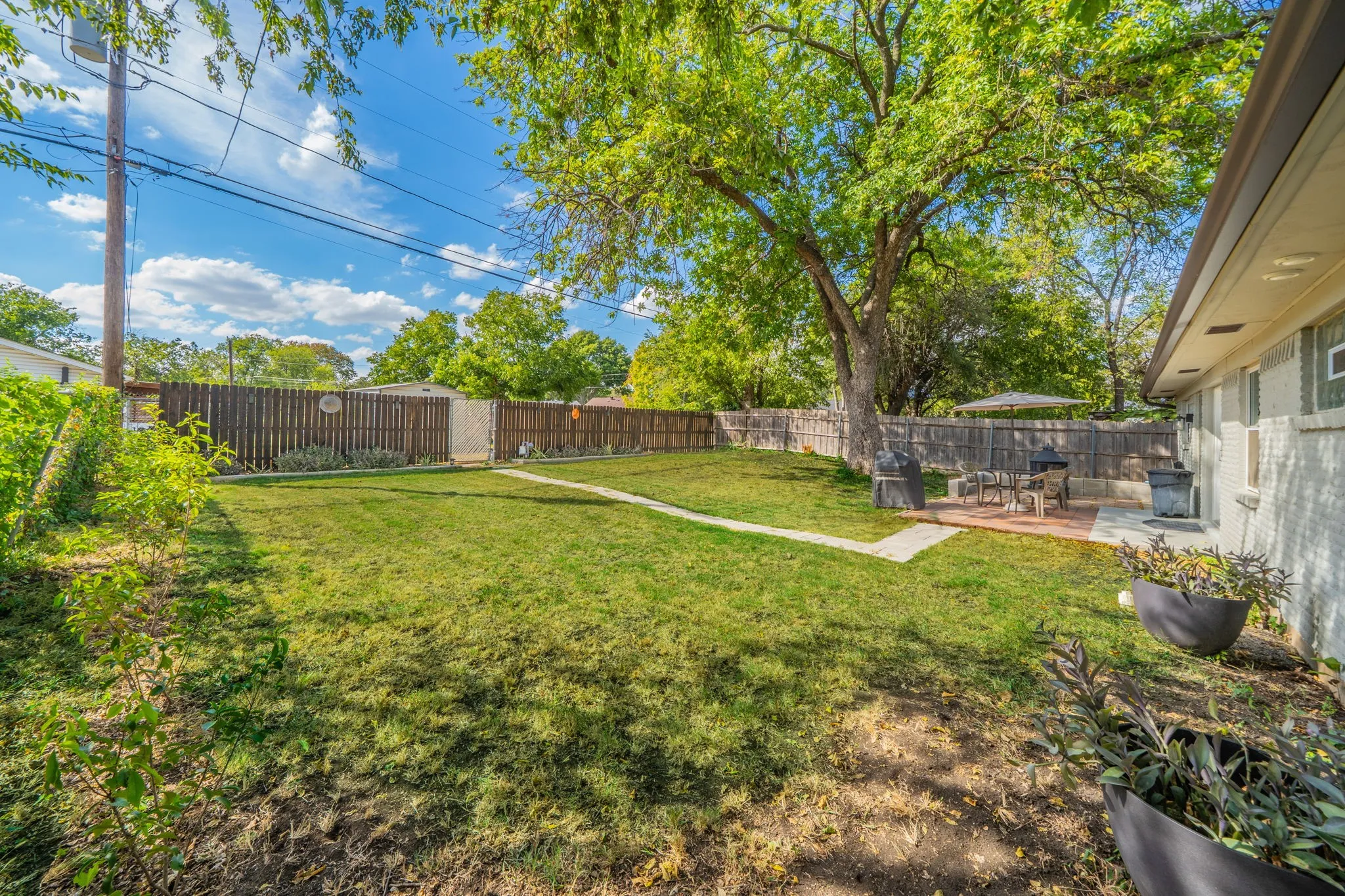 Expansive backyard with a manicured lawn, perimeter fencing, mature trees, and a paved patio area