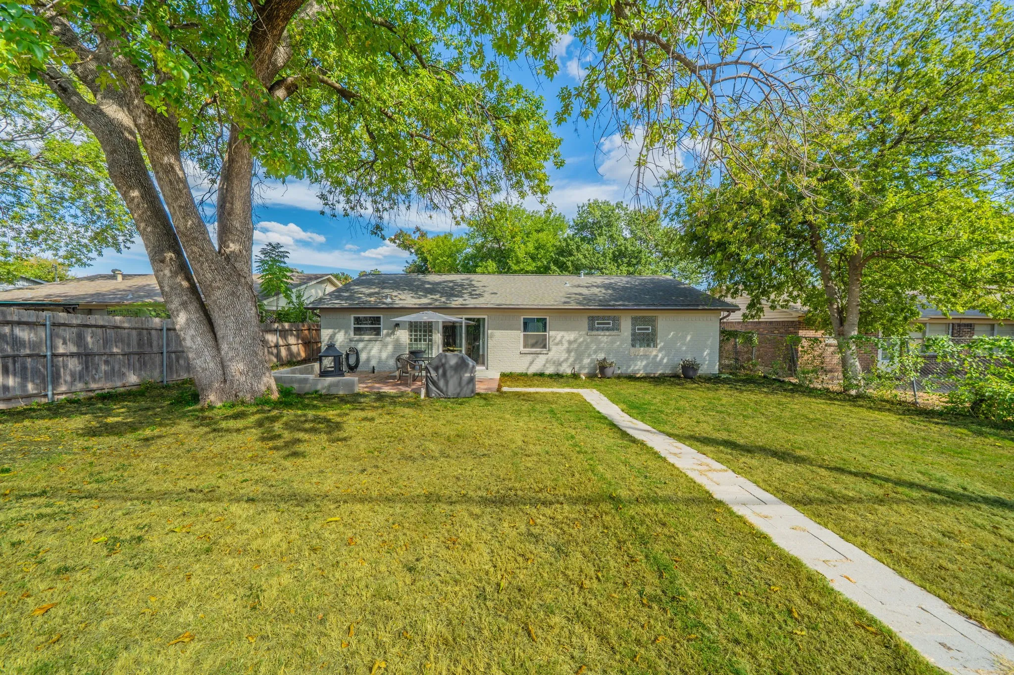 Expansive backyard featuring a concrete patio, mature trees, a privacy fence, and a concrete pathway