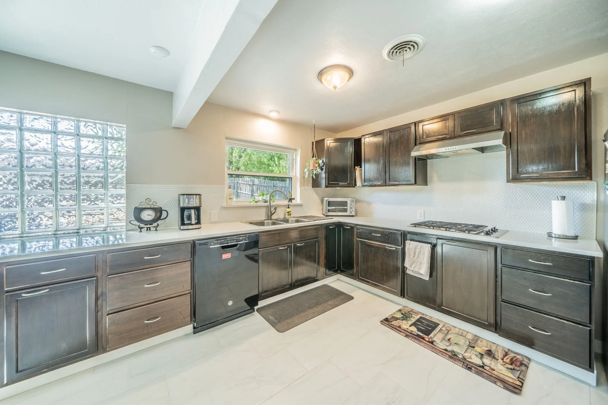 Large kitchen featuring wood cabinetry, quartz countertops, a glass block partition, a gas stovetop, and a stainless steel range hood