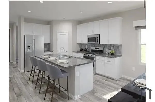 Expansive kitchen with a central island, recessed lighting, wood-finish flooring, white cabinetry, and stainless steel appliances