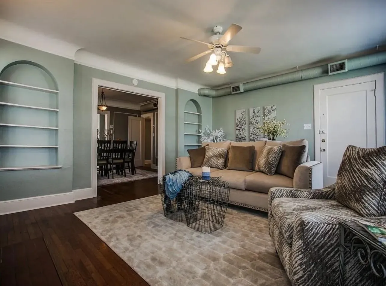 Wood-finish flooring, recessed built-in shelving, ceiling fan with integrated lighting, and an arched entryway