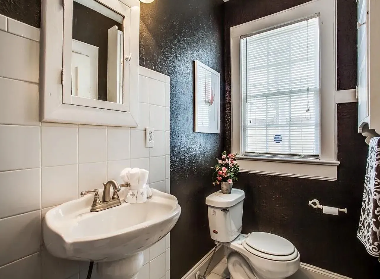 White ceramic tiled walls, pedestal sink, window with blinds, and wall-mounted medicine cabinet
