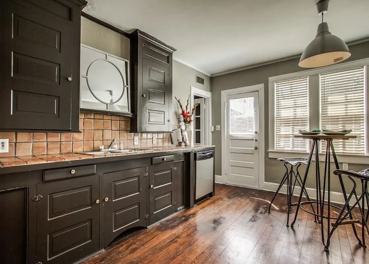 Hardwood flooring, dark wood cabinetry, tile backsplash, built-in dishwasher, and a paneled door
