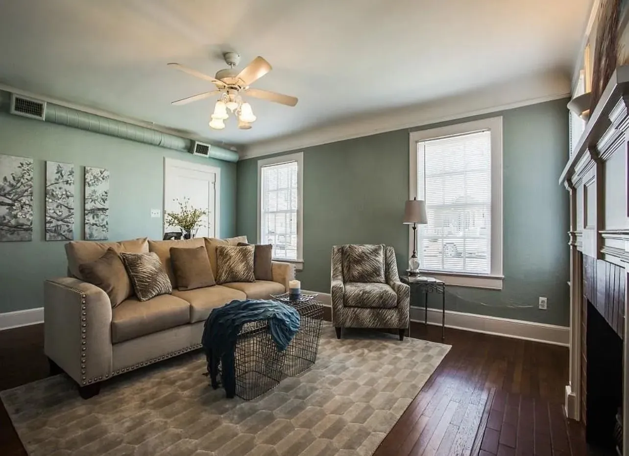 Hardwood flooring, painted walls, ceiling fan with integrated lighting, multiple windows, and a built-in fireplace with mantel
