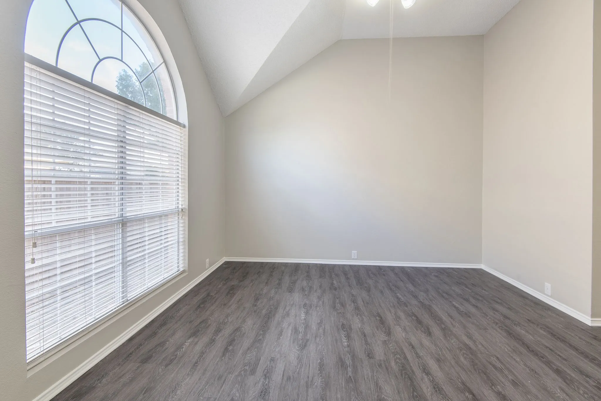 Vaulted ceiling with a ceiling fan, arched window with horizontal blinds, wood-finish flooring, and neutral wall paint