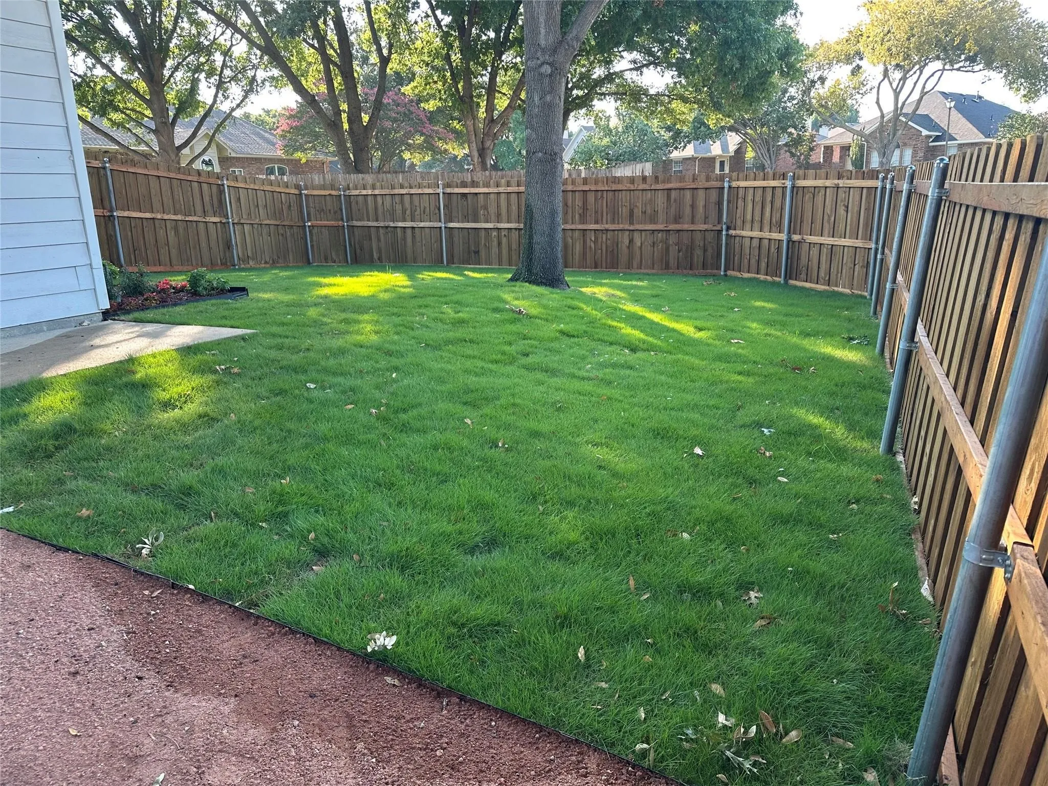 Manicured lawn with a mature tree, bordered by a wood privacy fence with metal posts