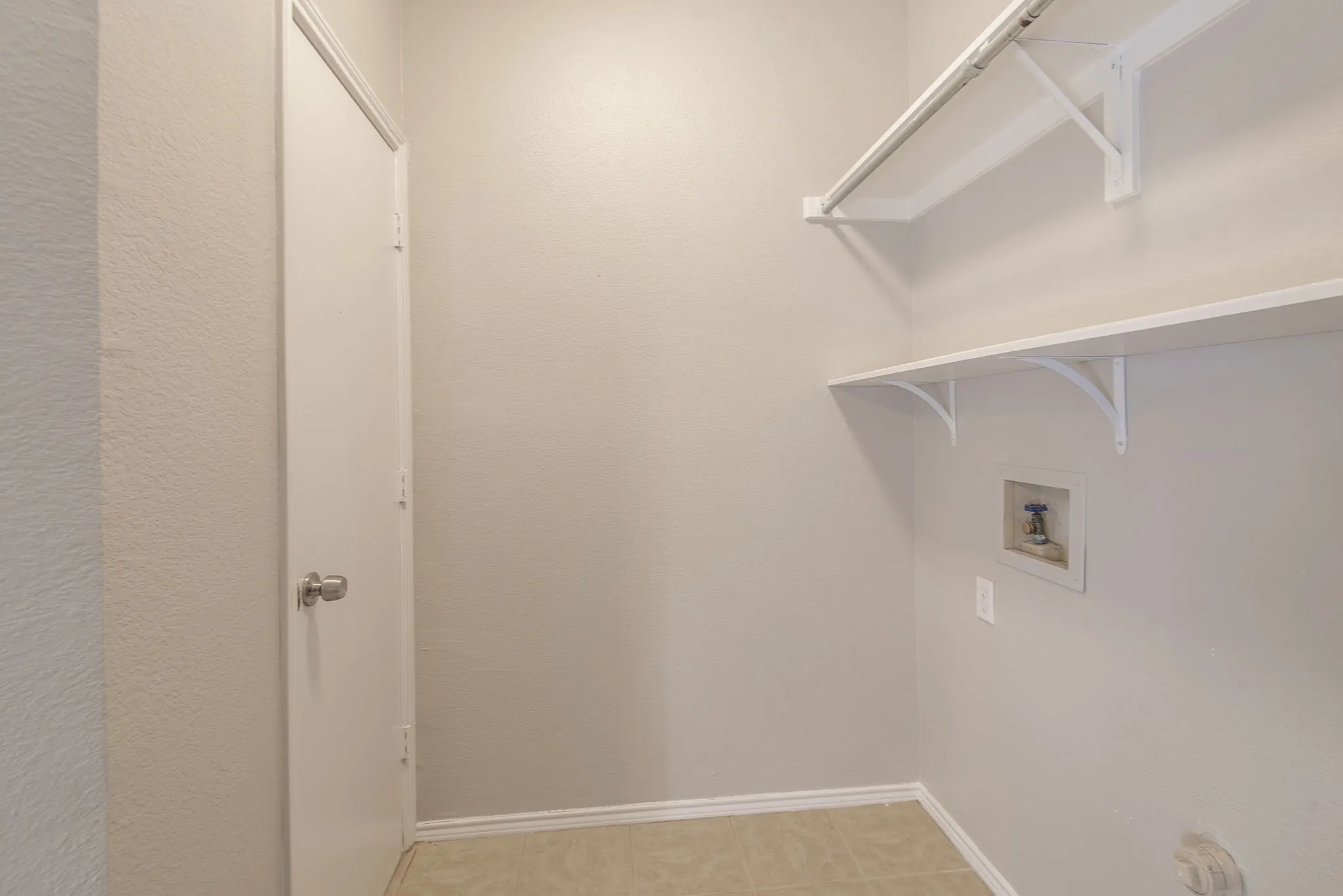 Utility room featuring light-toned walls, tile flooring, and a white door with a polished chrome doorknob