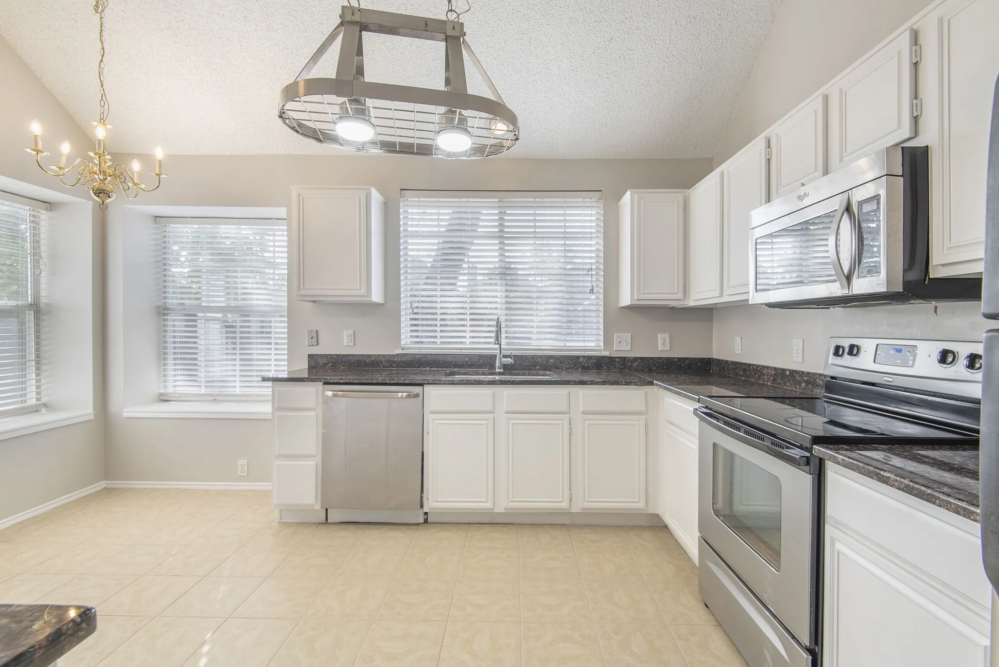 Kitchen featuring vaulted ceilings, white cabinetry, dark countertops, and stainless steel appliances