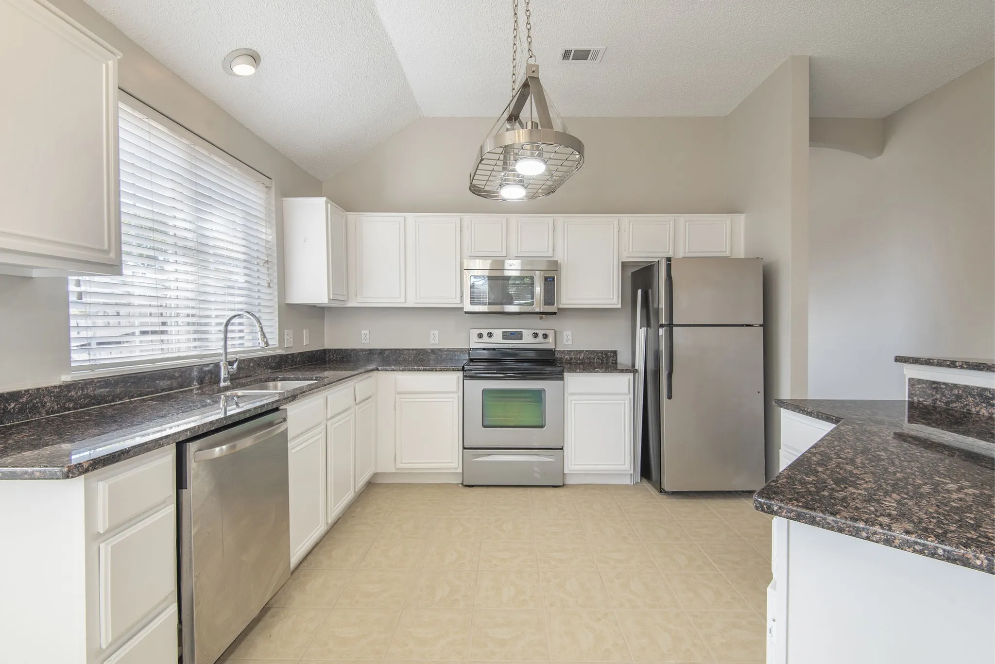 Kitchen featuring white cabinetry, dark speckled countertops, stainless steel appliances, and a vaulted ceiling with decorative lighting