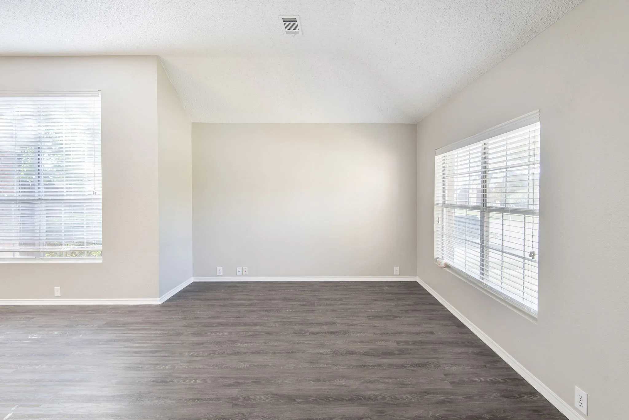 Vaulted ceiling, wood-finish flooring, neutral wall tones, and multiple windows