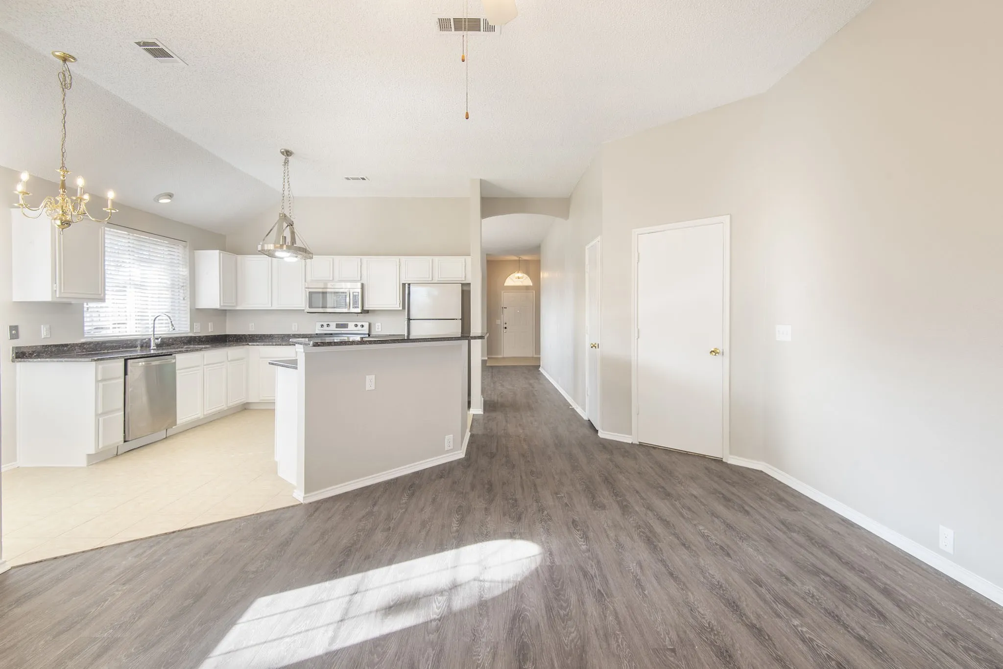 Vaulted ceiling, wood-finish flooring, white cabinetry, stainless steel appliances, and a breakfast bar