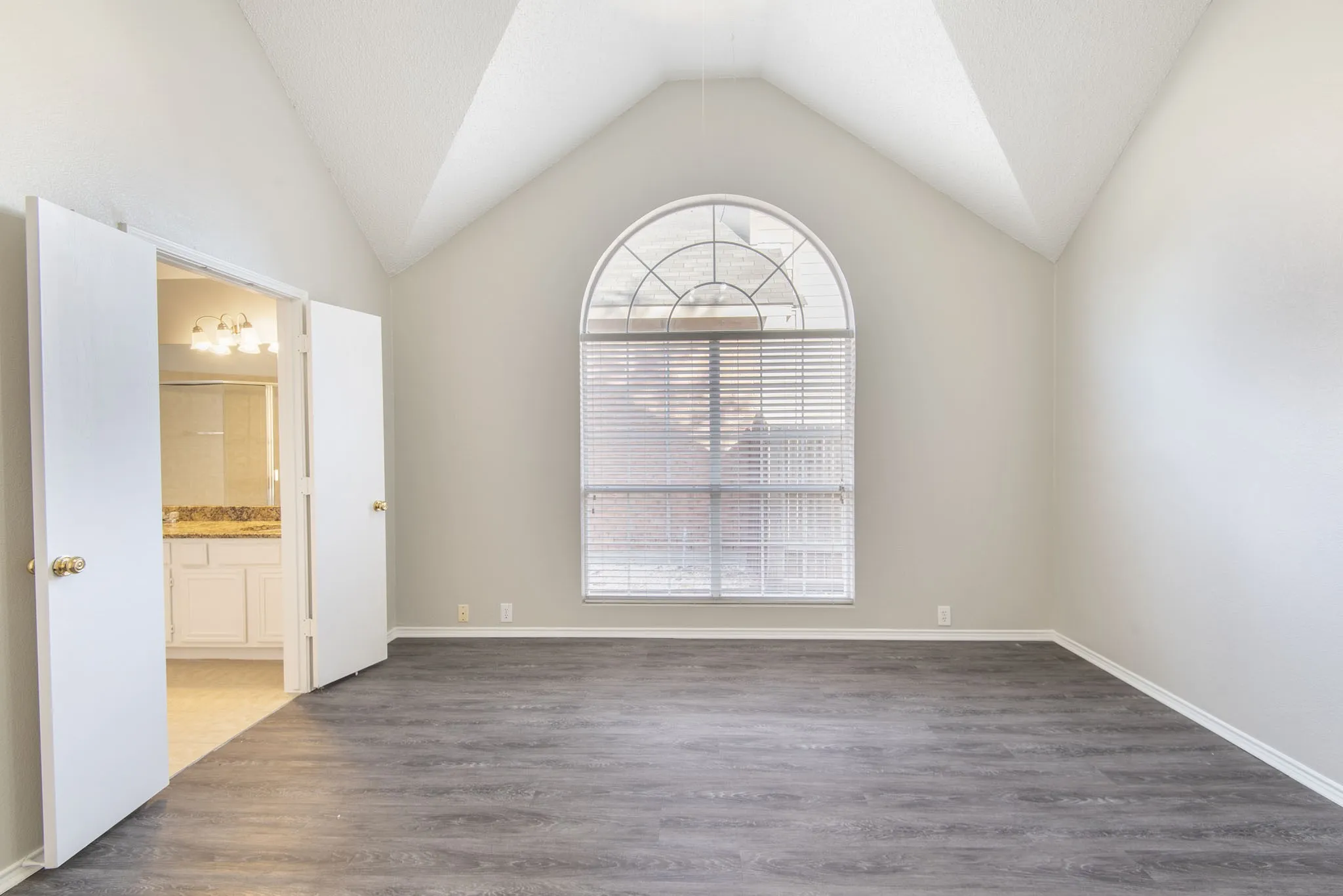 Vaulted ceilings, wood-finish flooring, and an arched window with horizontal blinds
