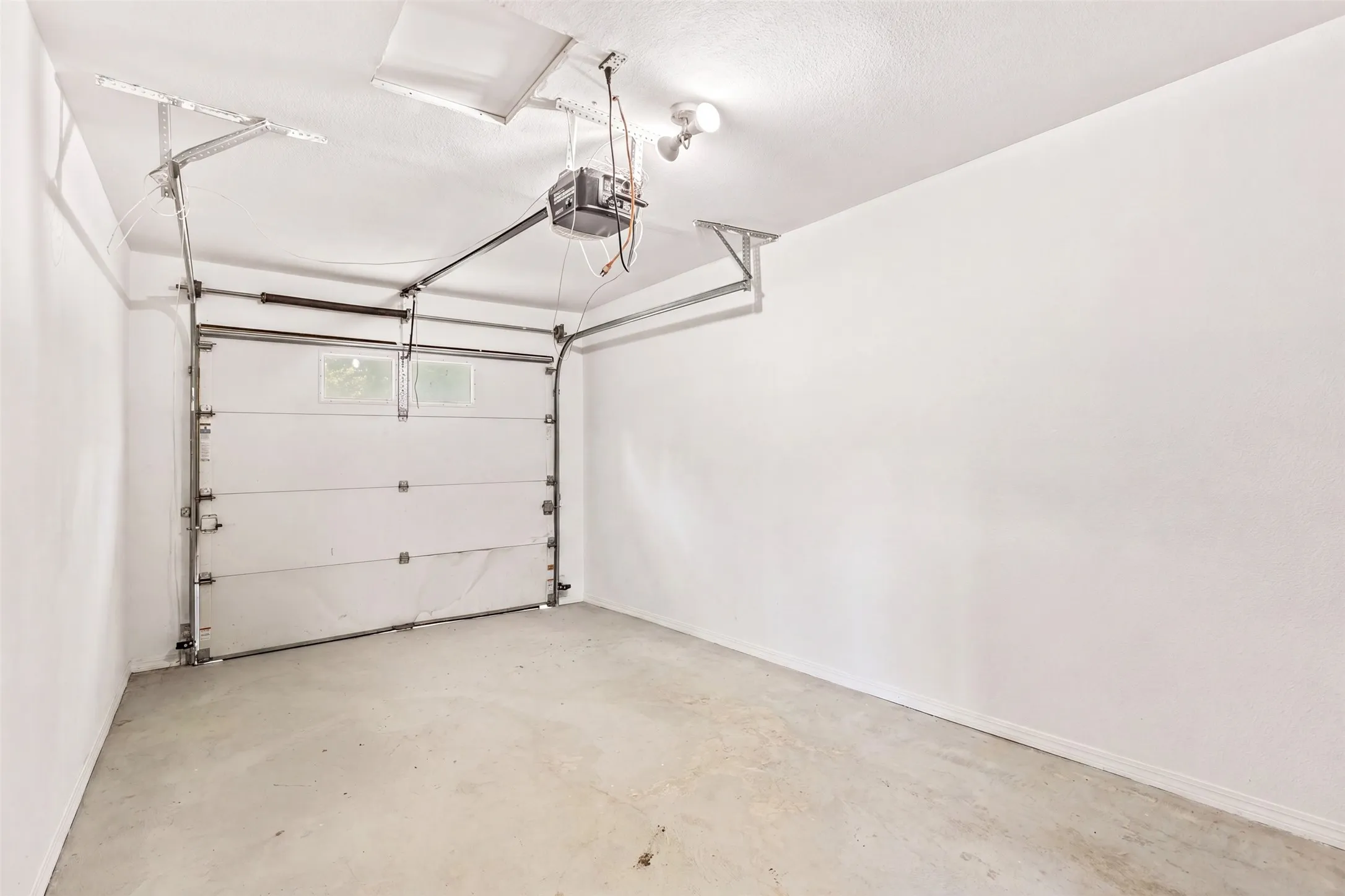 Concrete flooring, white walls, overhead lighting, garage door, and garage door opener