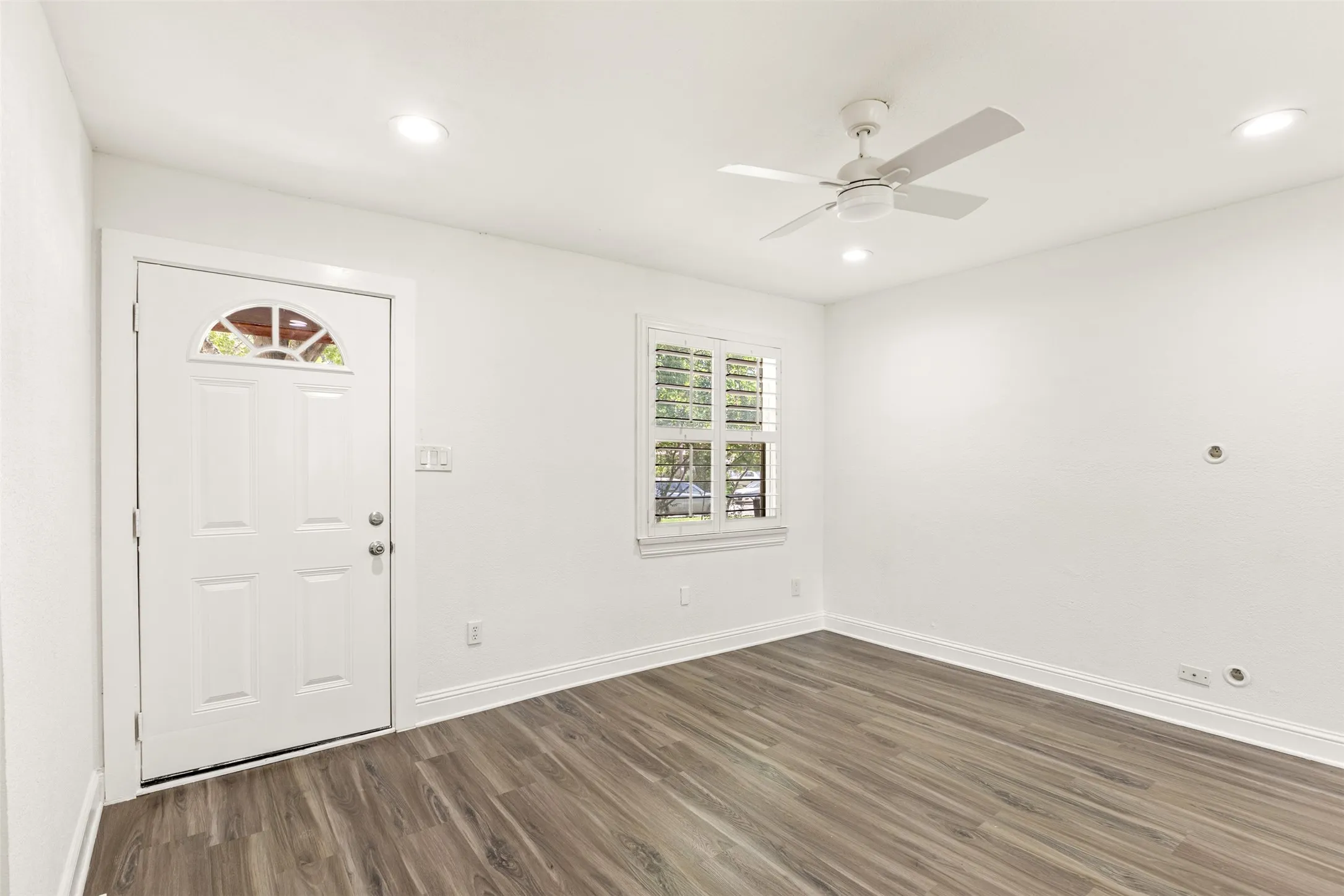 Wood-finish flooring, white paneled door with arched transom, and white window shutters