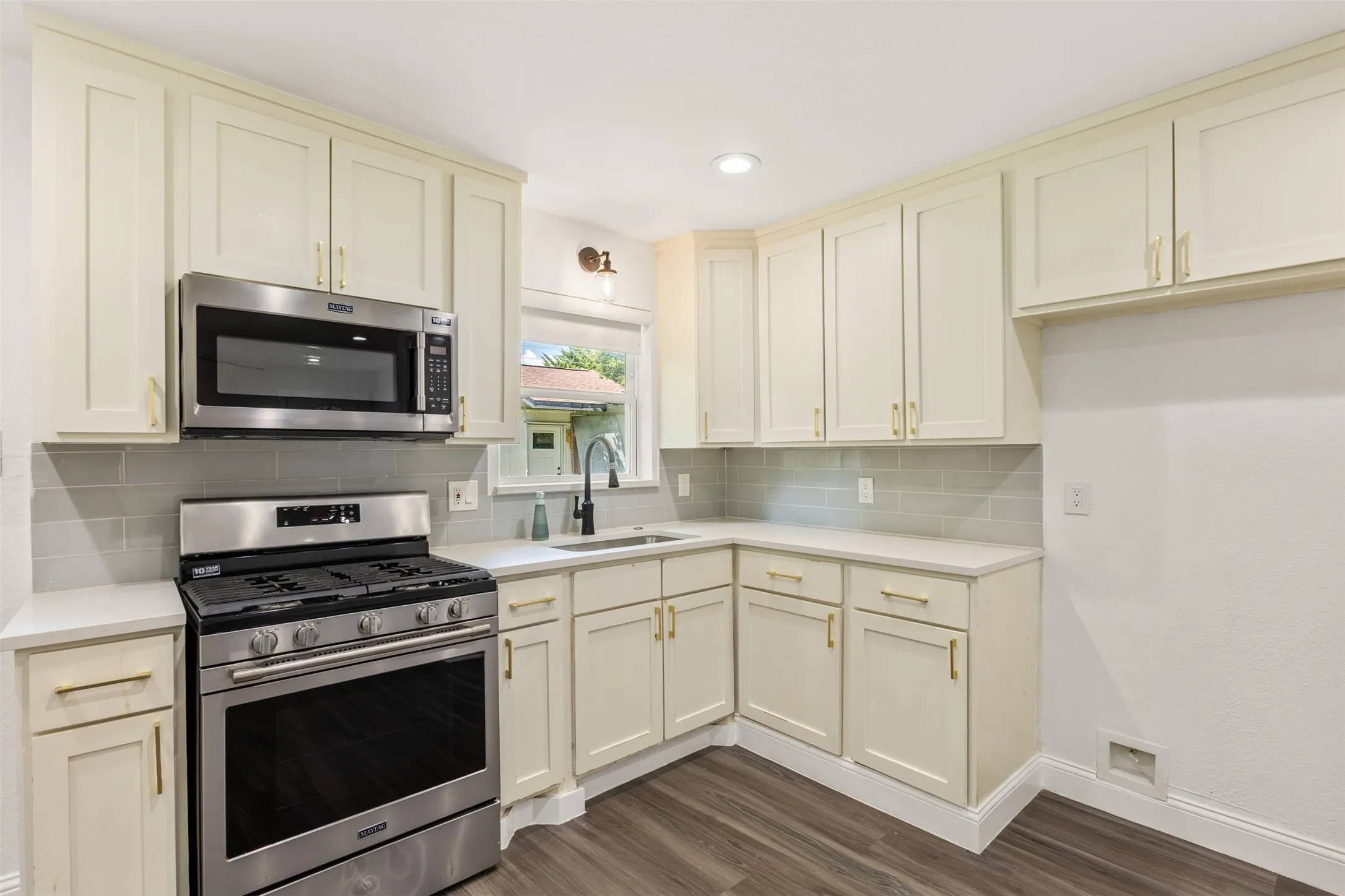 Modern kitchen featuring light-toned cabinetry, stainless steel appliances, a subway tile backsplash, and wood-finish flooring