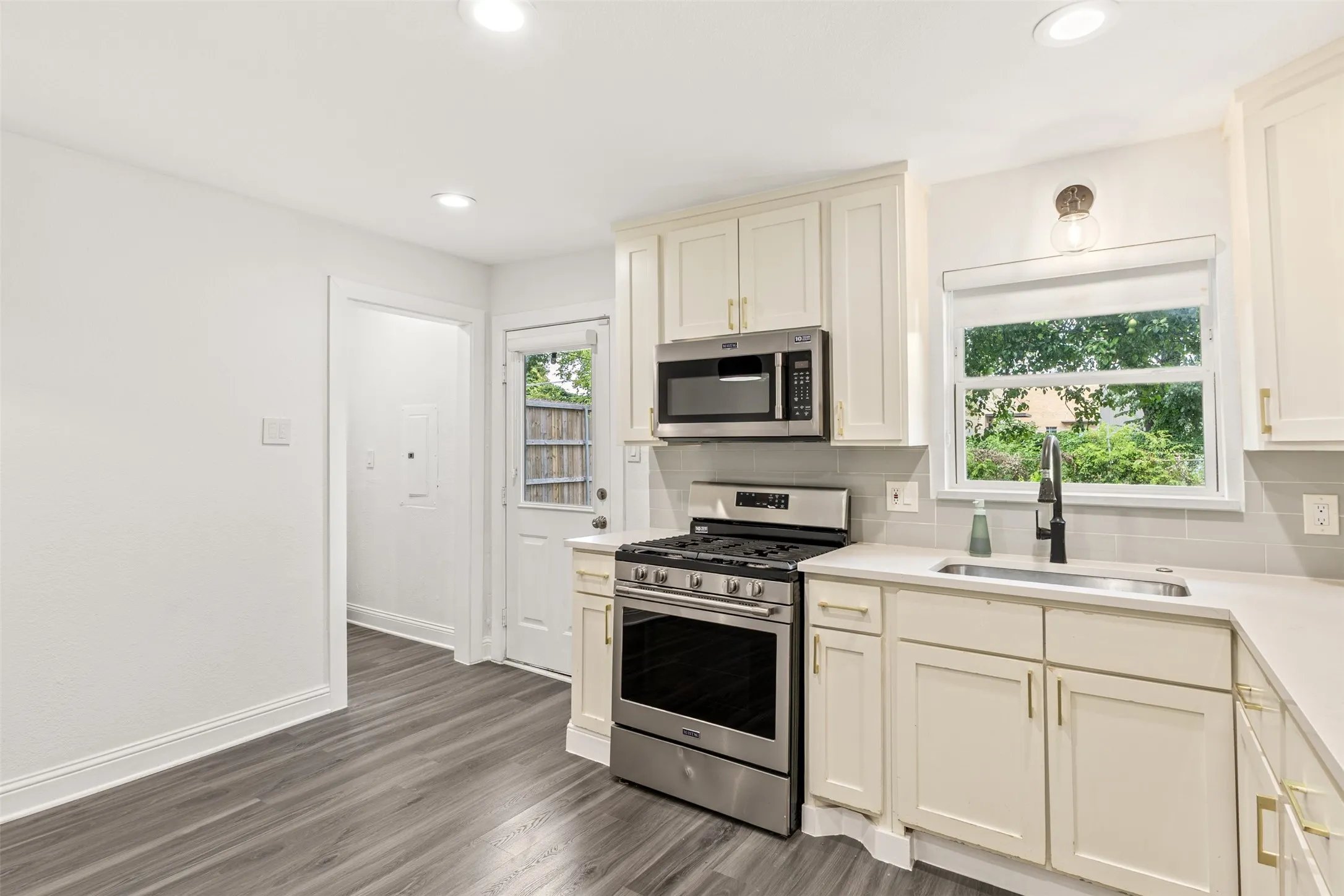 Kitchen featuring wood-finish flooring, stainless steel appliances, solid surface countertops, a tile backsplash, and recessed lighting