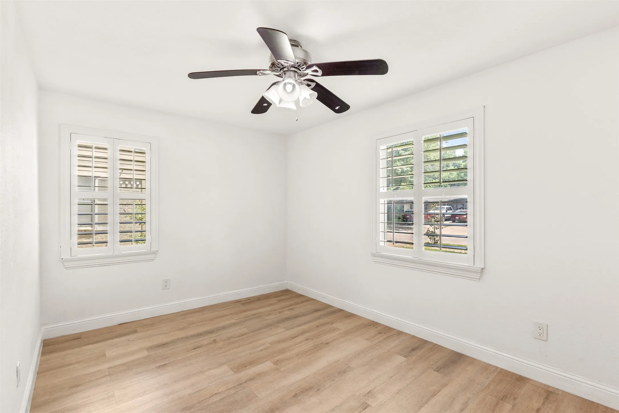 Bright interior with two windows, plantation shutters, wood-finish flooring, and a ceiling fan with integrated lighting