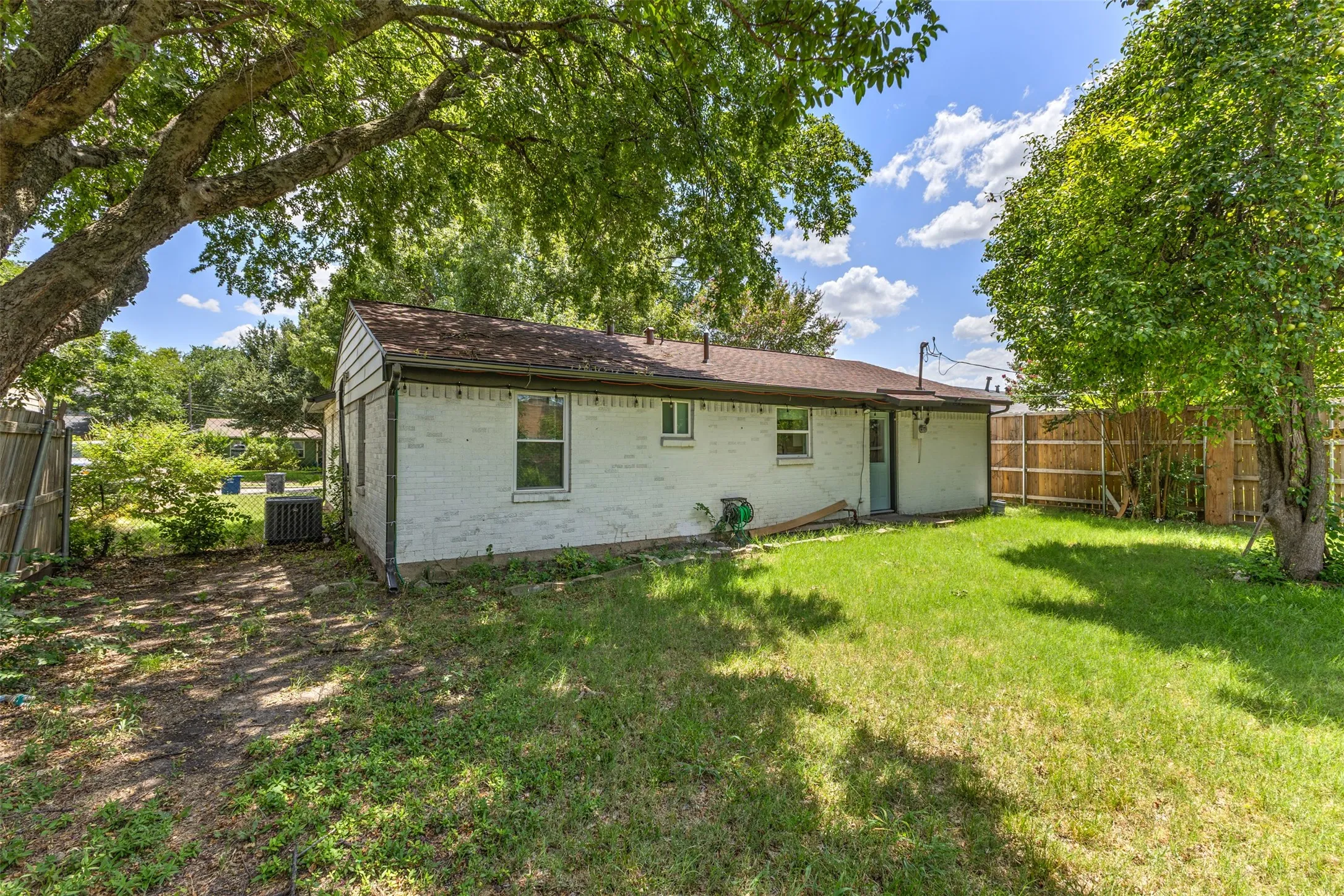 Expansive backyard featuring a partial privacy fence, mature trees, and a brick exterior with multiple windows