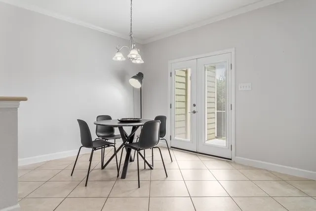 Neutral-toned tile flooring, crown molding, double French doors with glass panels, and a polished chrome chandelier