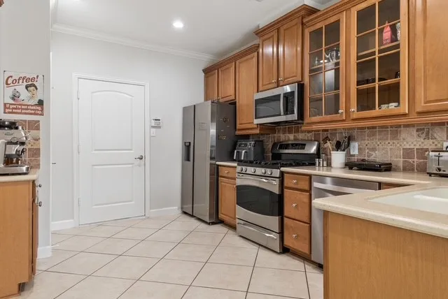 Kitchen featuring wood cabinetry, stainless steel appliances, tiled flooring, and a tiled backsplash