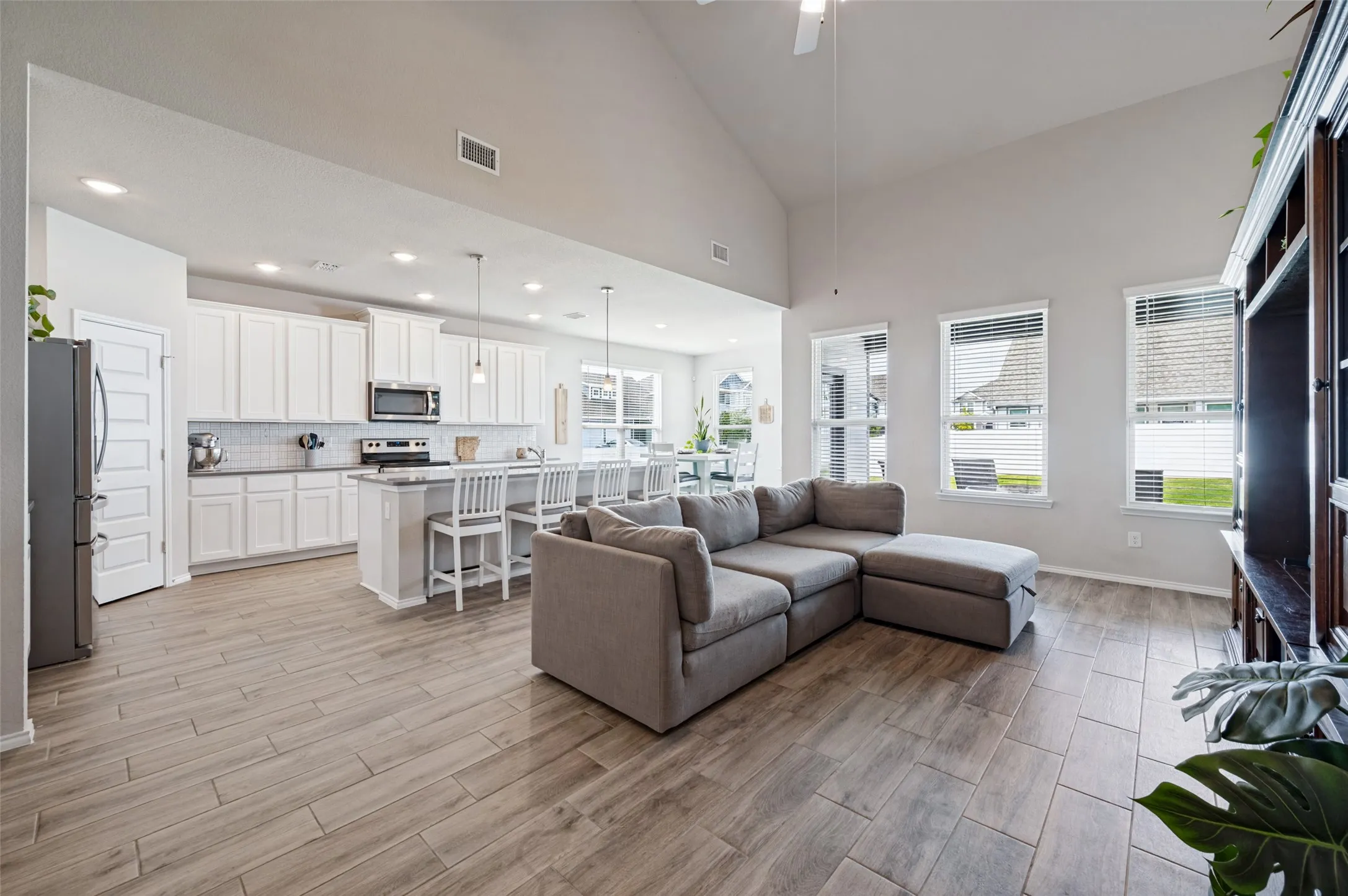 Vaulted ceilings with a ceiling fan, wood-finish flooring, white cabinetry, a kitchen island with pendant lighting, and multiple windows with blinds