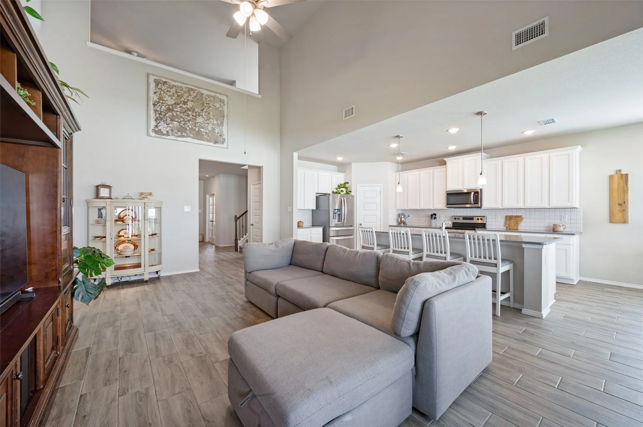 Two-story ceiling, wood-finish flooring, white kitchen cabinetry, stainless steel appliances, and pendant lighting