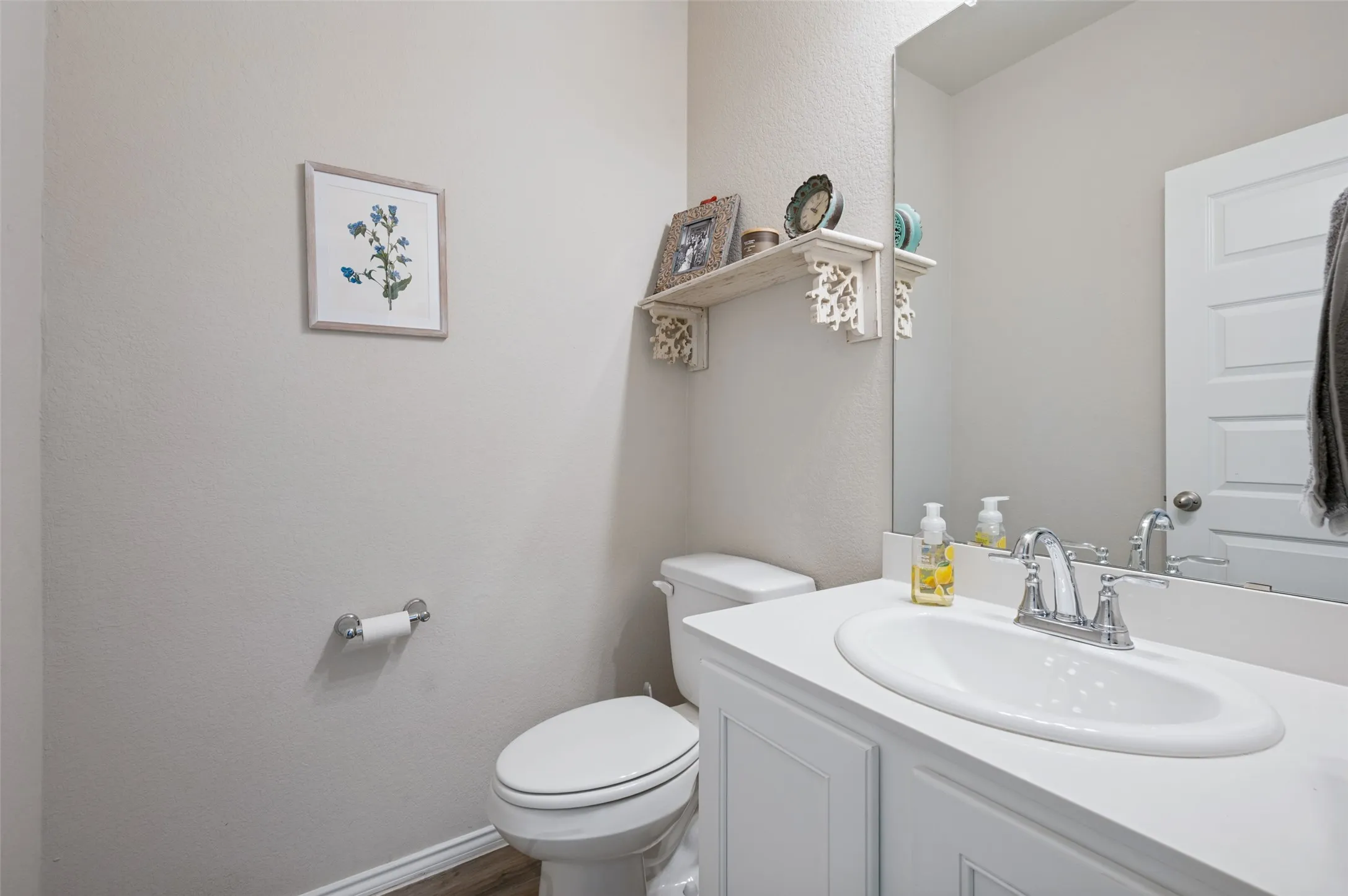 White vanity with an integrated sink and chrome faucet, large wall-mounted mirror, and wood-finish flooring