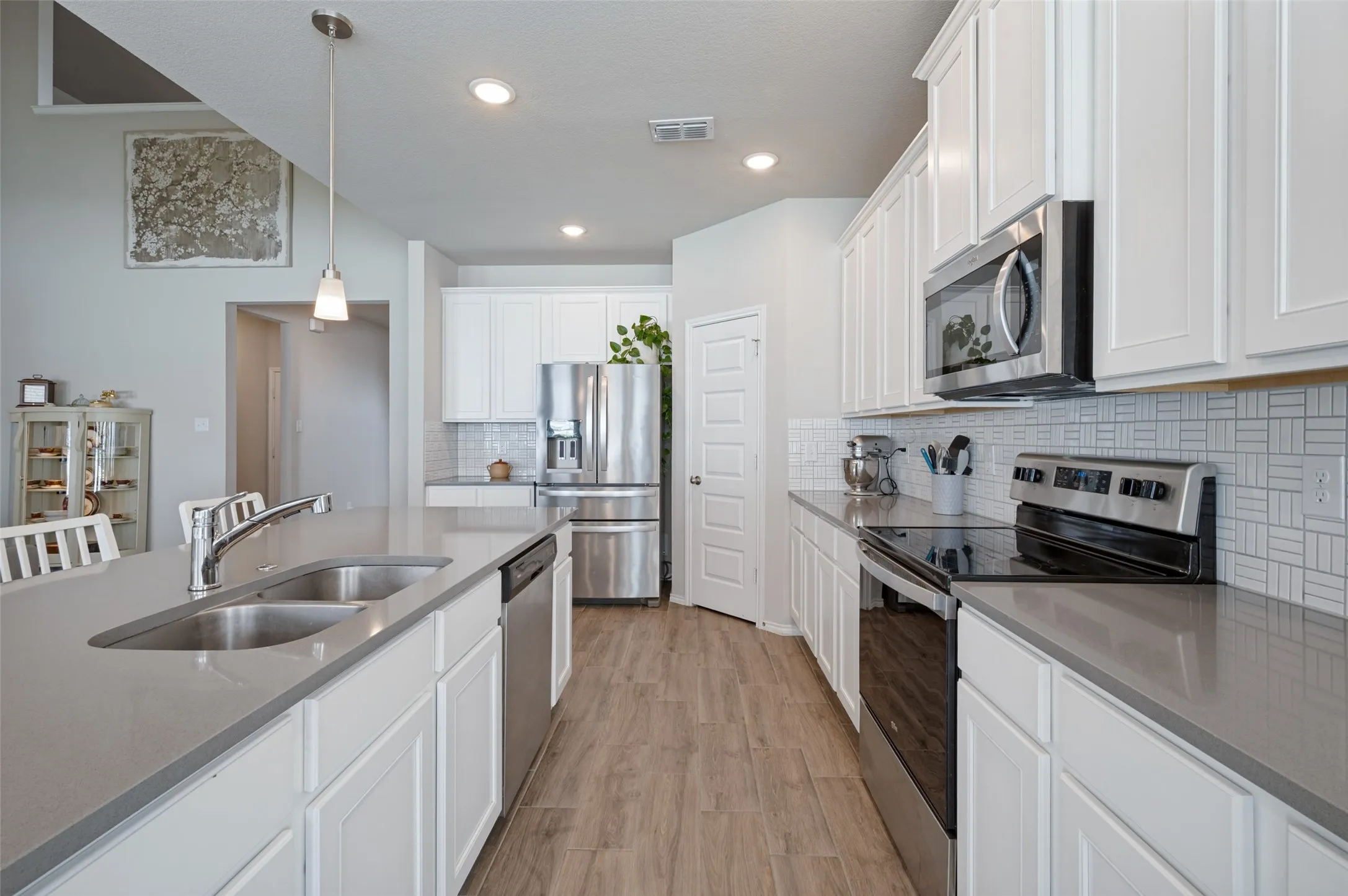 Kitchen featuring an island with dual basin sink, white cabinetry, integrated stainless steel appliances, light gray countertops, and wood-finish flooring