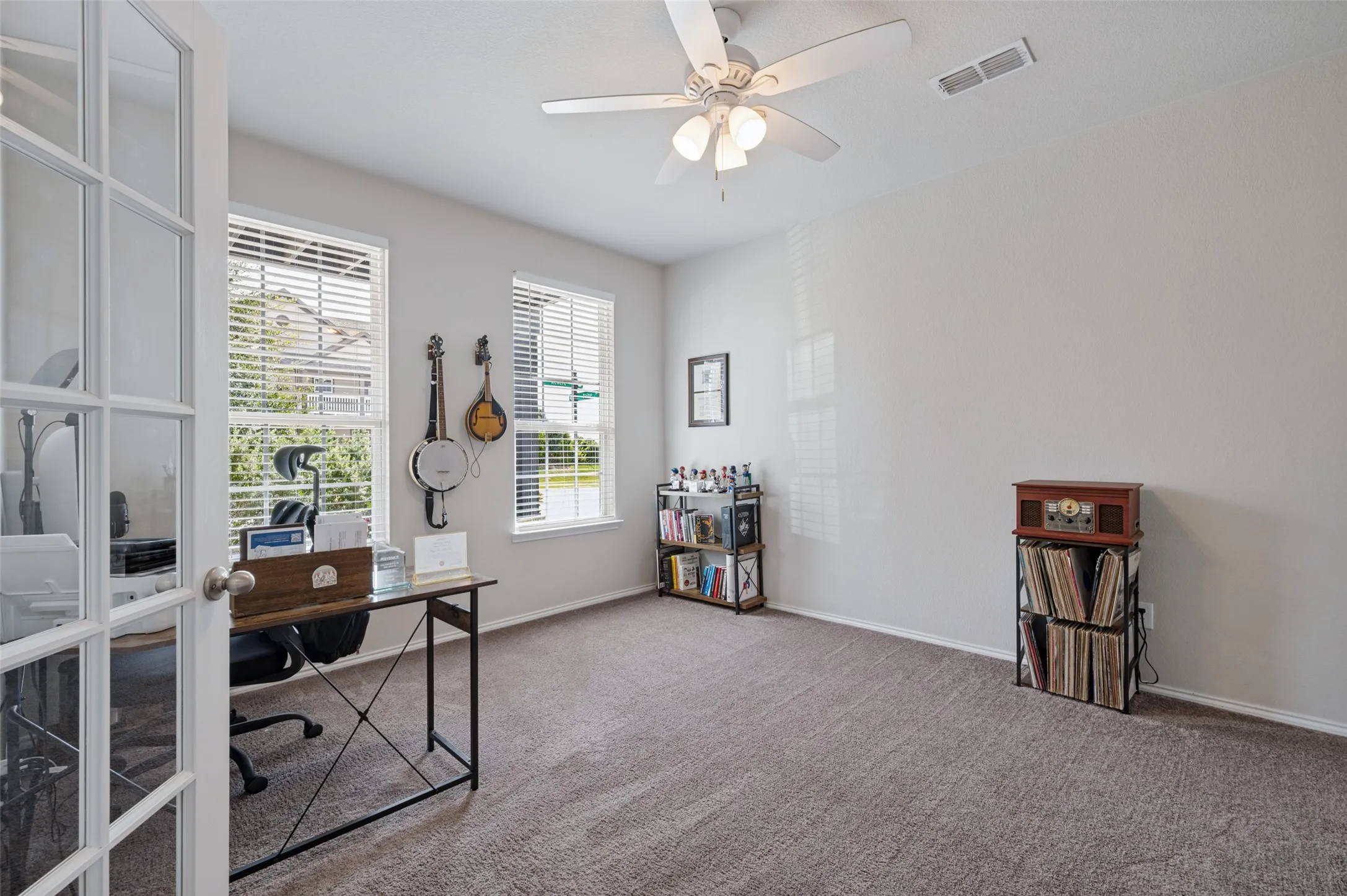 Room with carpeted flooring, two windows with blinds, a ceiling fan with integrated lighting, and a French door entry