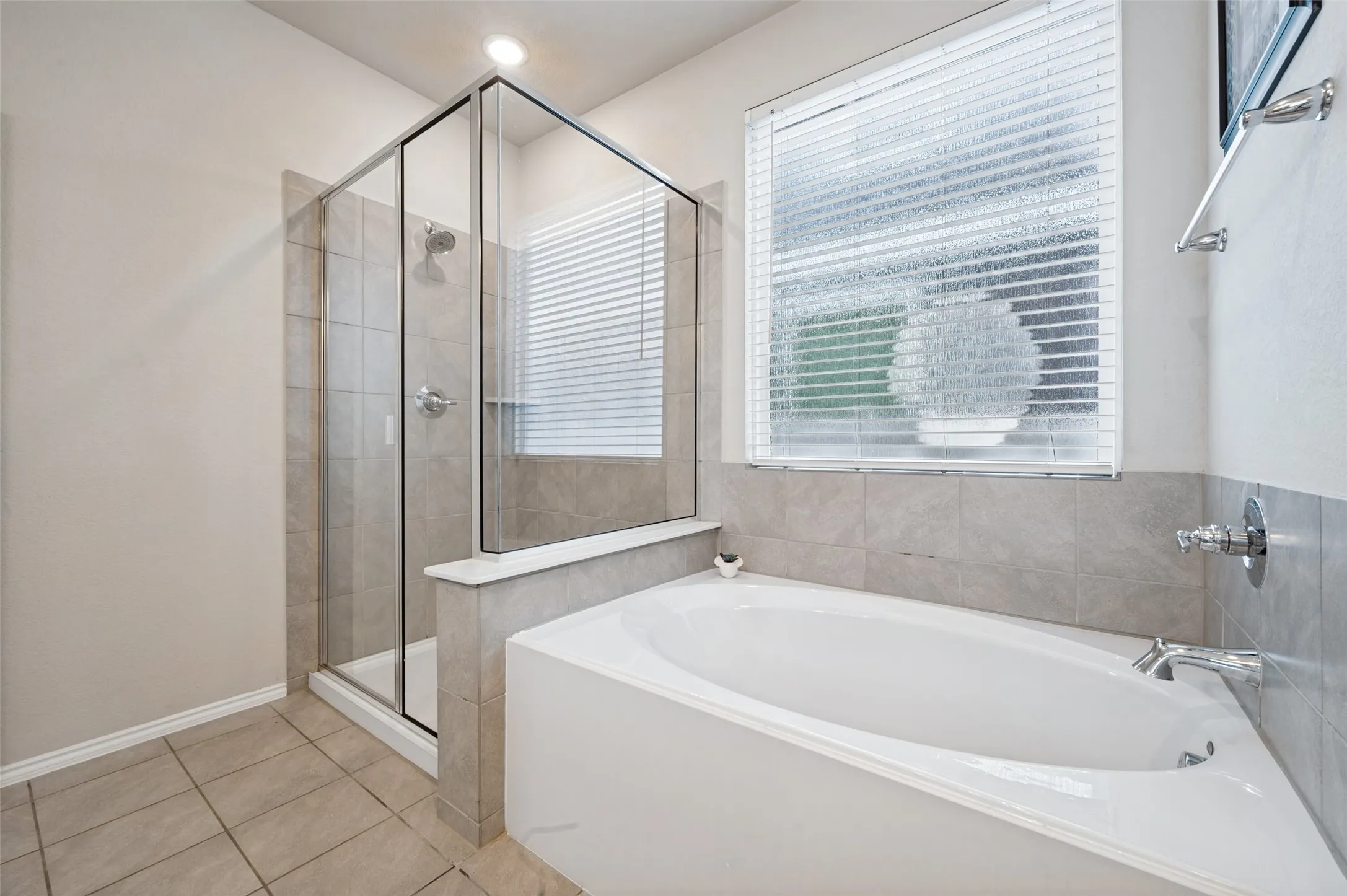 Recessed lighting illuminates the glass-enclosed shower with a rainfall showerhead, accompanied by a spacious soaking tub