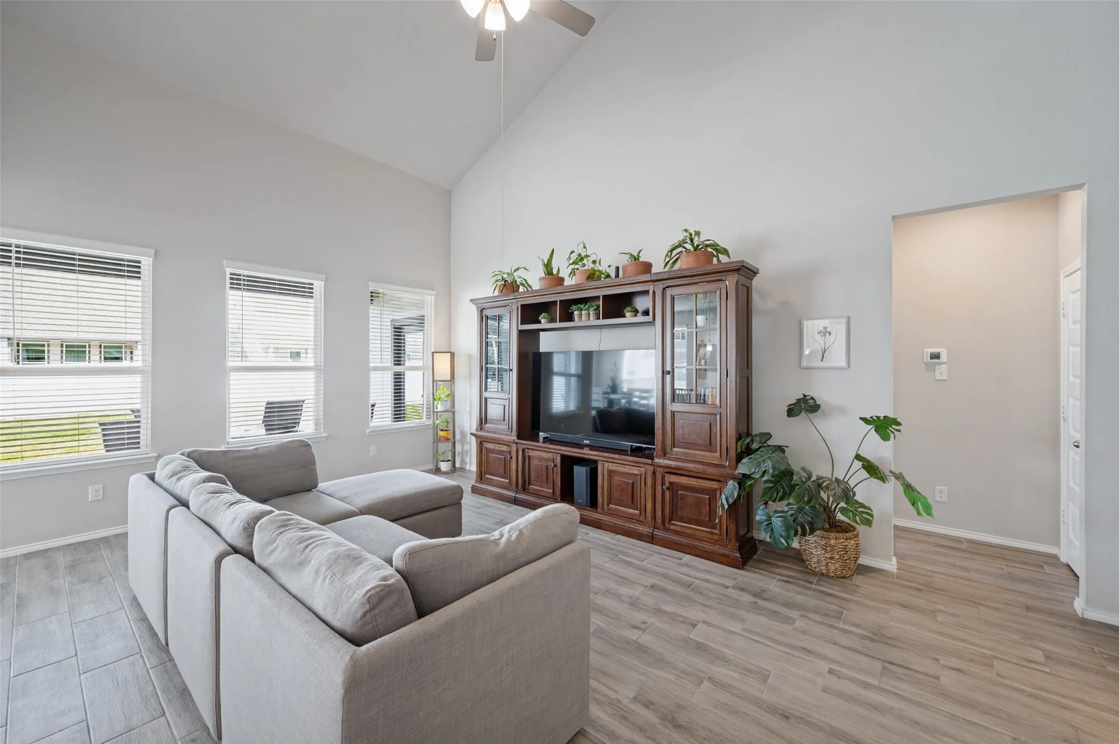 Vaulted ceiling, ceiling fan, multiple windows with blinds, wood-finish flooring, and light wall color