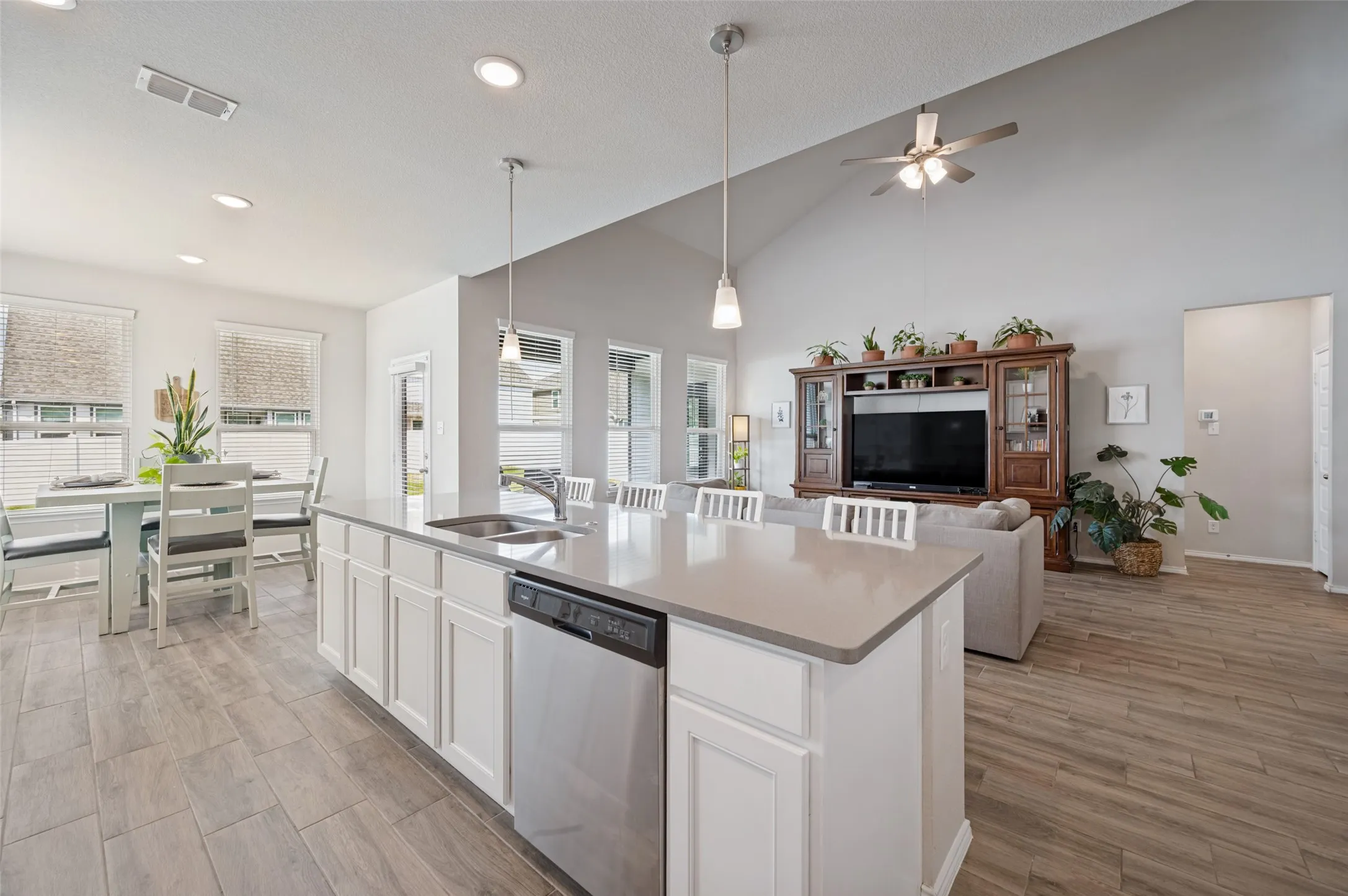 Kitchen island with integrated sink and dishwasher, recessed lighting, wood-finish flooring, vaulted ceiling, and multiple windows