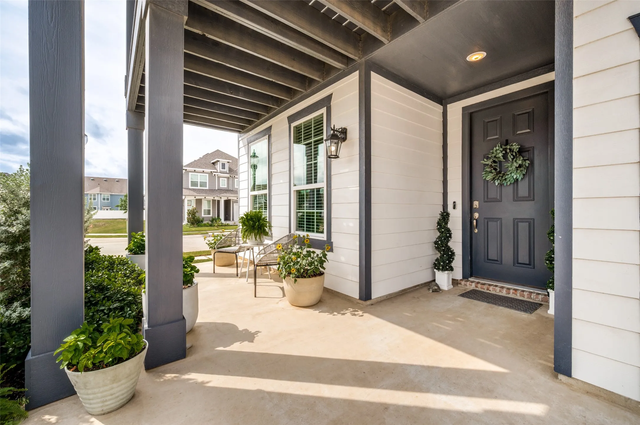 Covered porch featuring a dark grey entry door, horizontal siding, and large windows with white trim